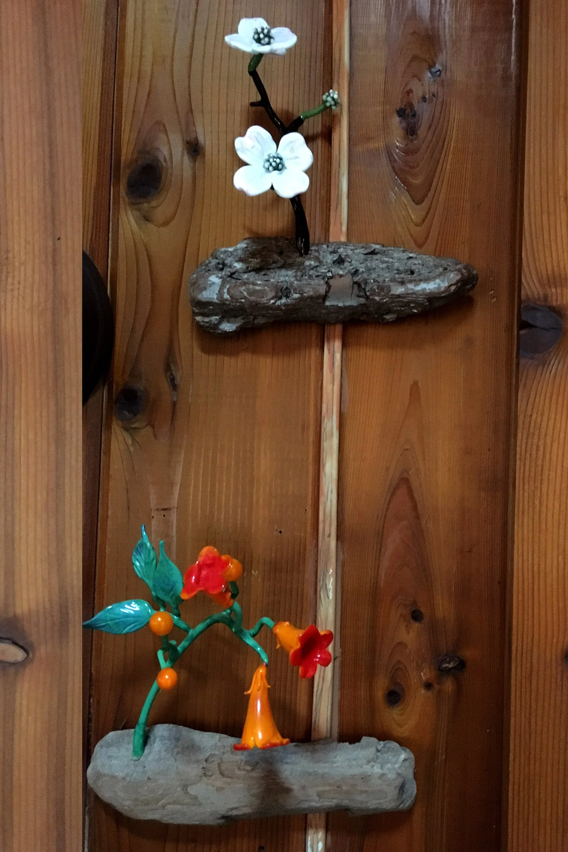 Decorative artificial flowers on a wooden wall, with a stone base at the bottom.