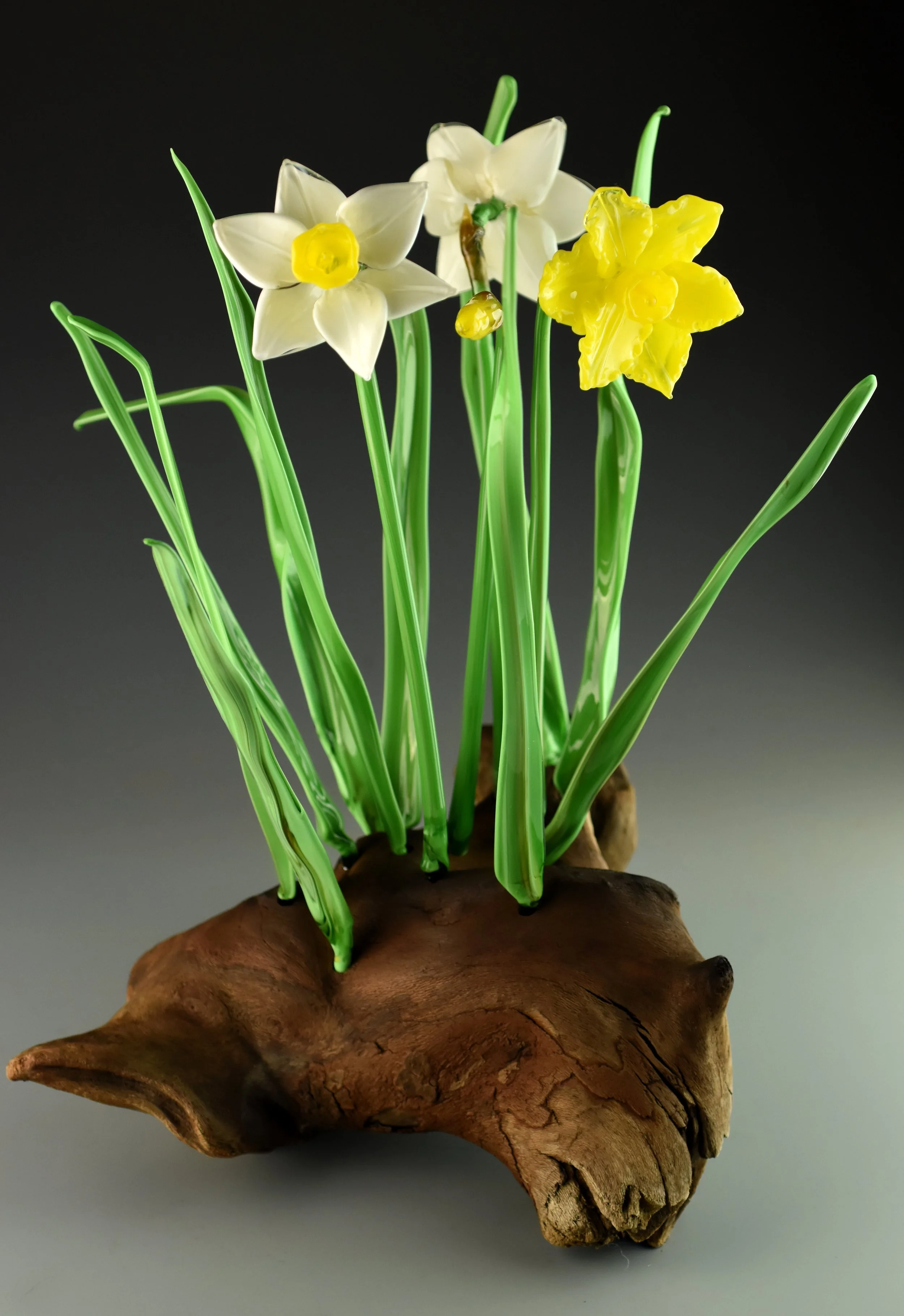 Artificial daffodil flowers in a wooden base against a dark background.