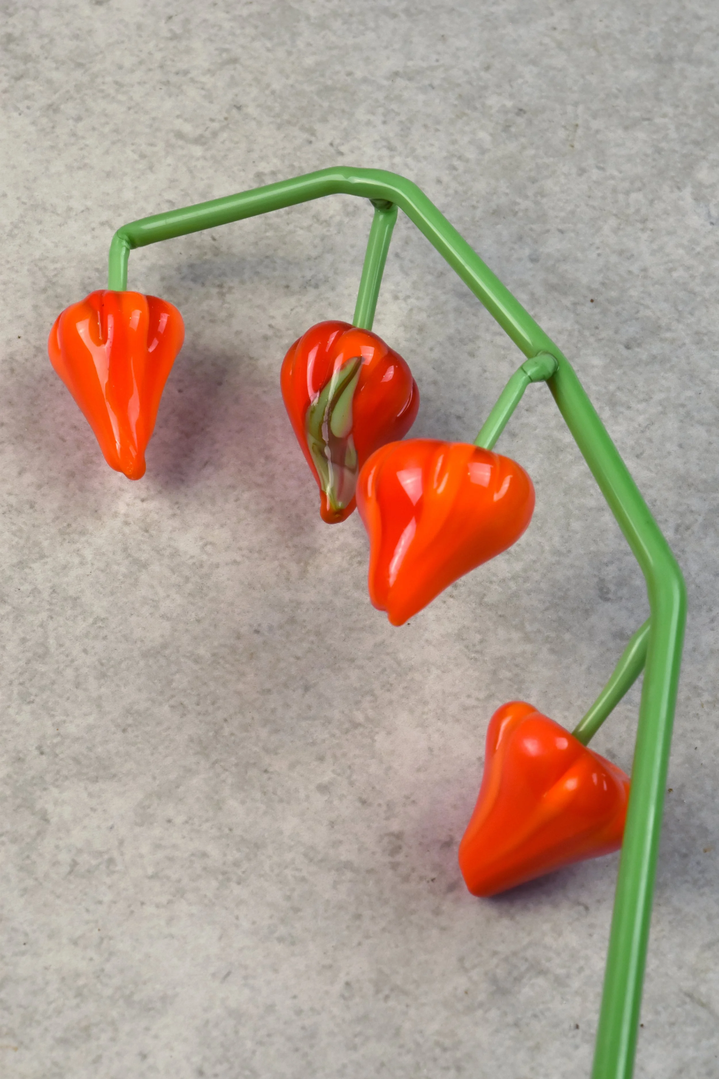 Colorful glass peppers on a green glass stem, set against a plain gray background.