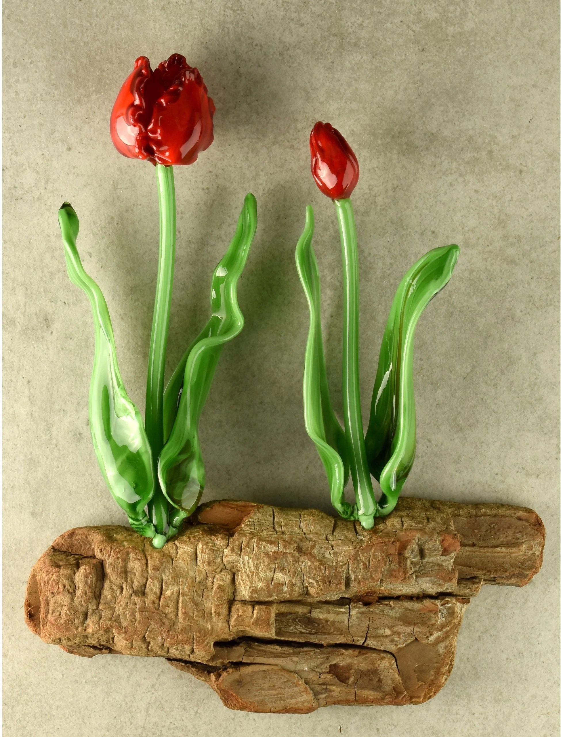 Glass sculpture of a red tulip flower with green stem and leaves, mounted on a piece of driftwood.
