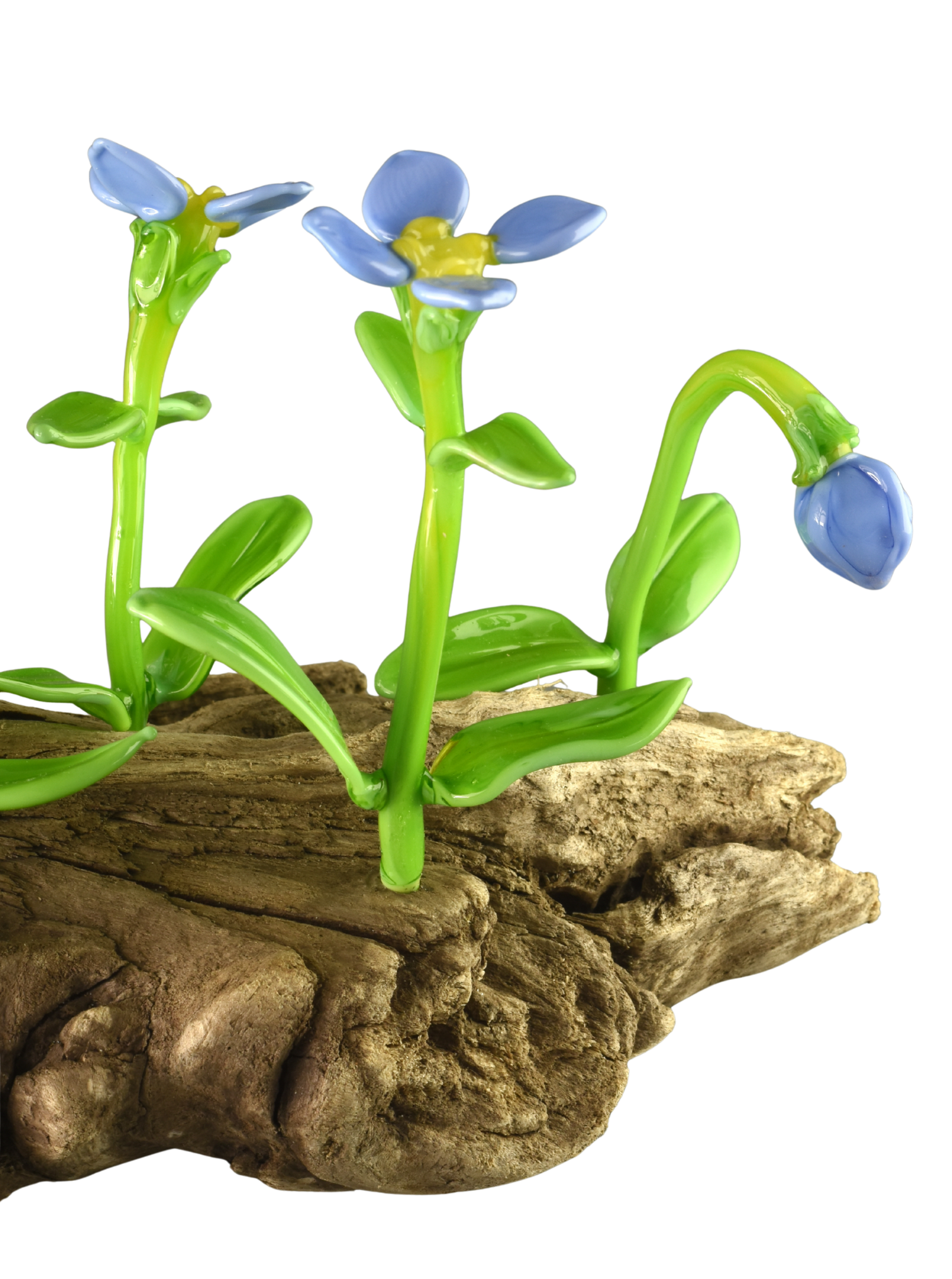 Glass sculpture of blue flowers with green stems, growing from a piece of wood. The sculpture mimics real plant growth, with three flowers at different stages of bloom.