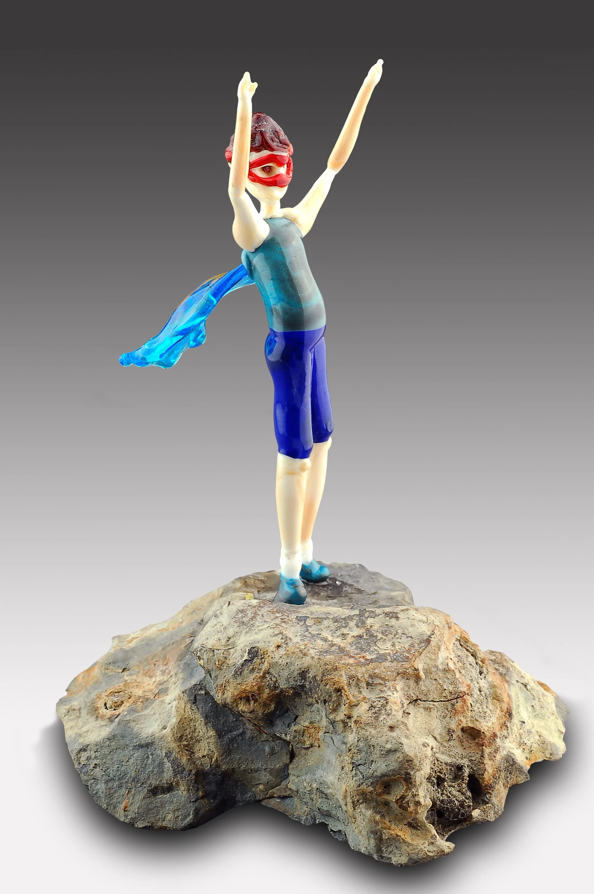 A colorful glass sculpture of a joyful boy on a large rock.