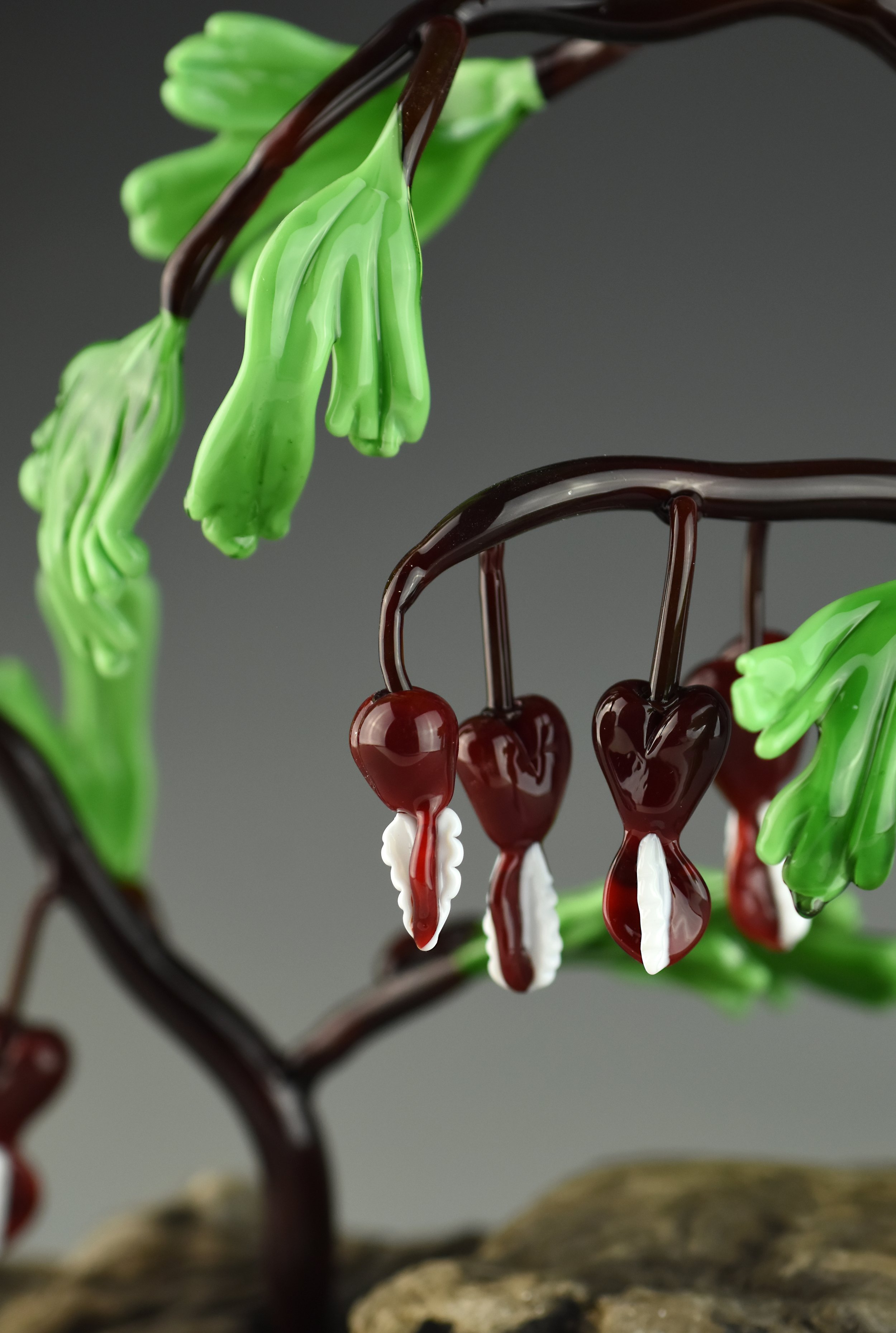 A decorative glass sculpture of a cherry tree with green leaves and red cherries, made of colored glass.