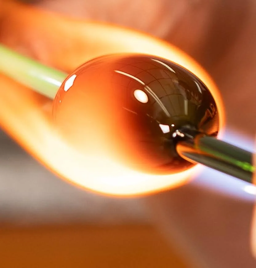 Close-up of a glass marble held by metal tweezers, glowing orange-hot from being heated or melted.