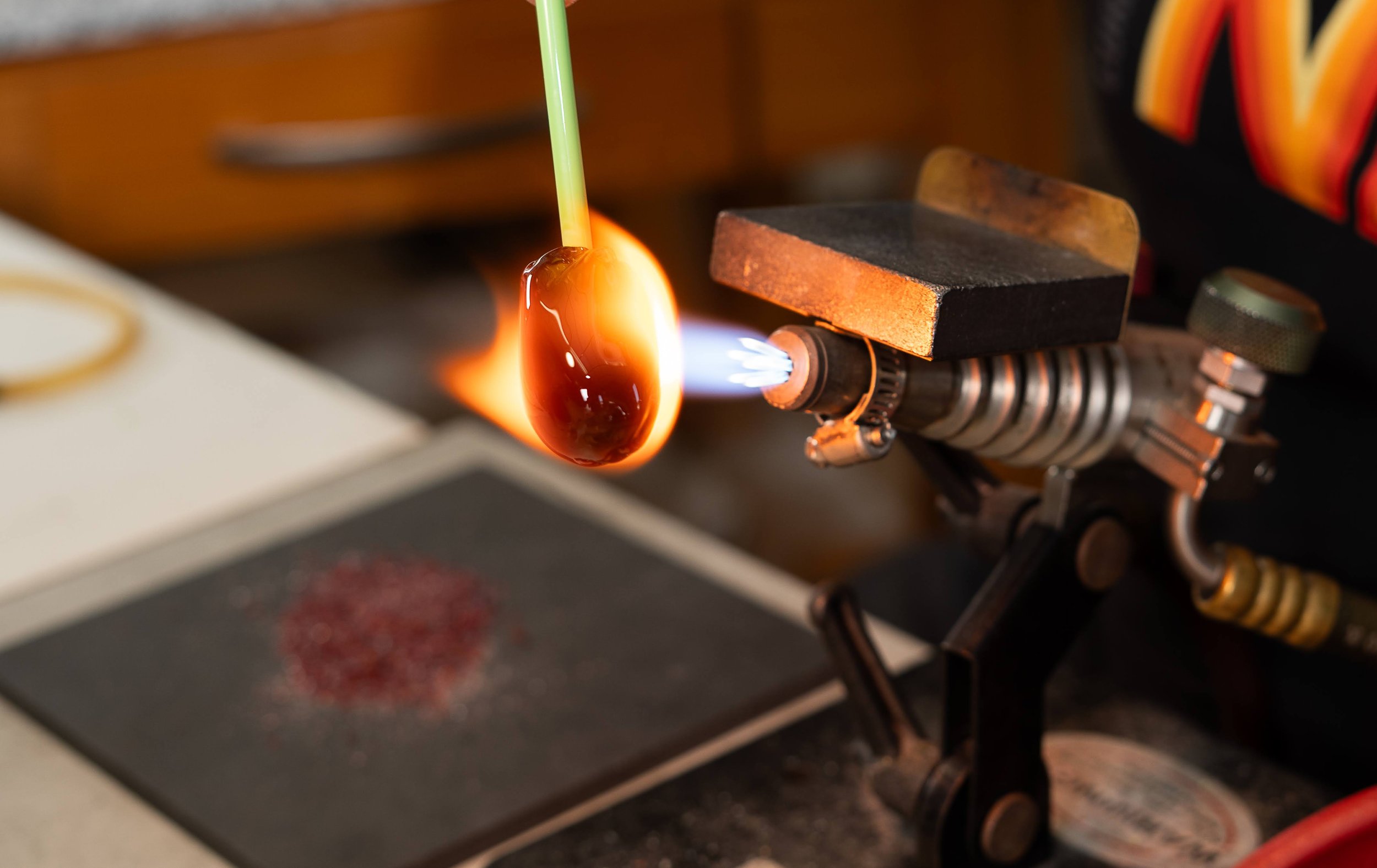 A glass object is being heated with a torch in a workshop or laboratory setting, with a flame and a workbench visible.