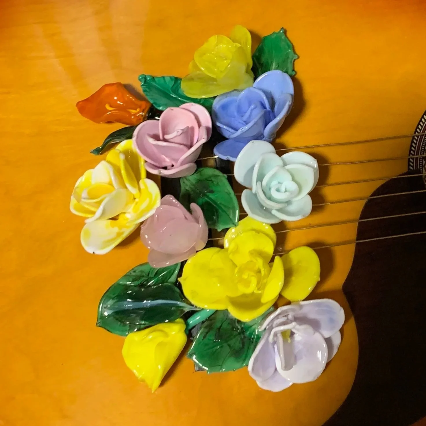 A decorative arrangement of colorful glass flowers, including roses and leaves, placed on a wooden surface.