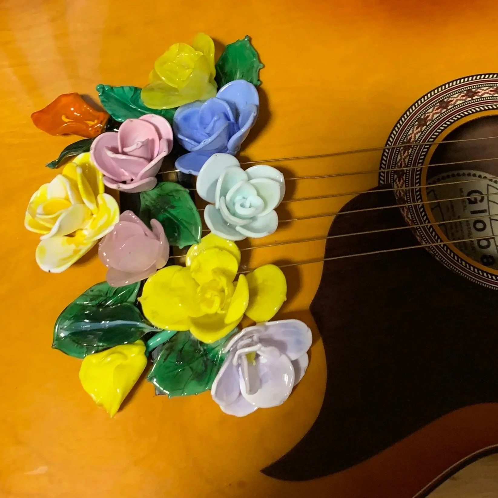 Colorful glass flower-shaped ornaments on a wooden surface, with part of a decorative ceramic or wooden object visible on the right side.