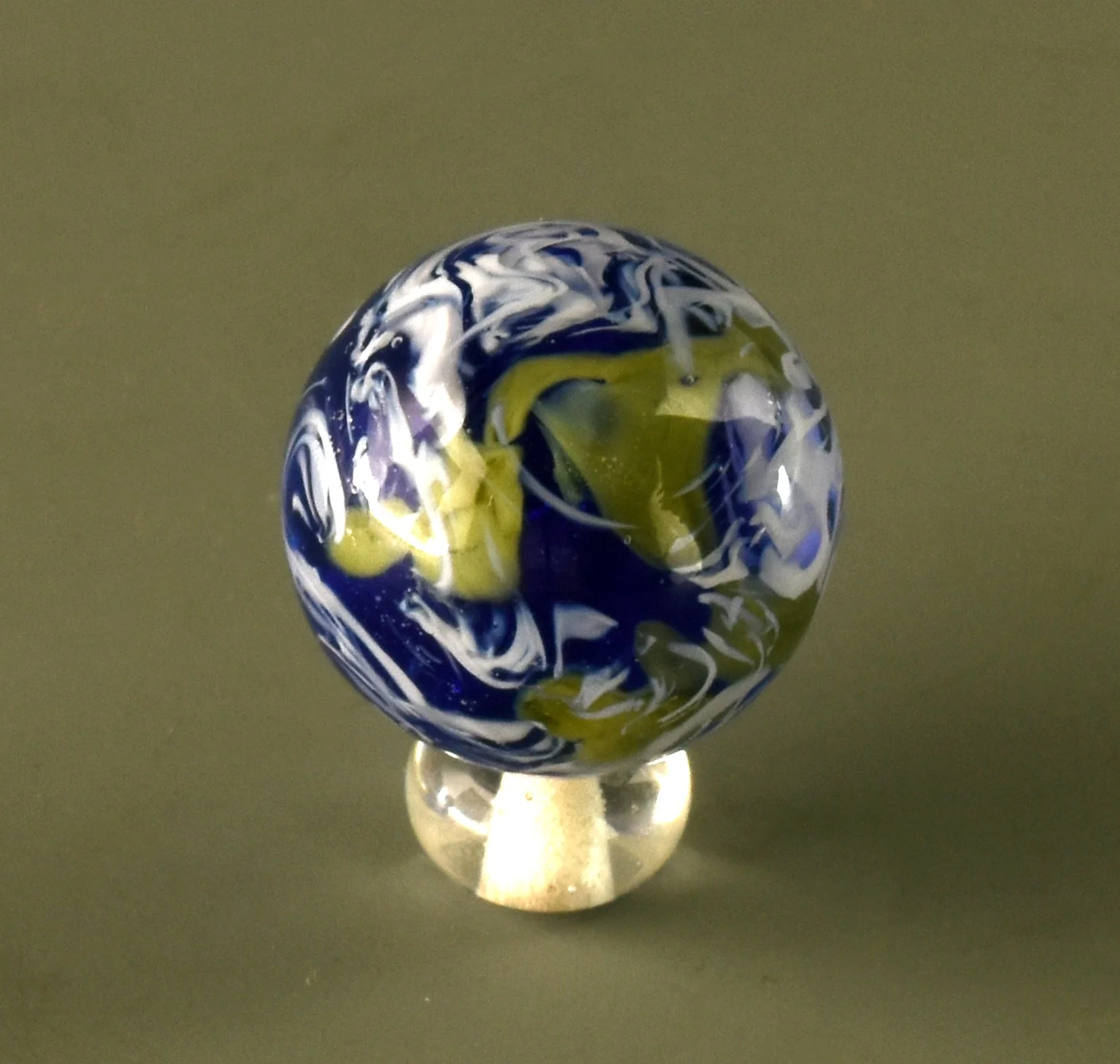 A marble with swirling patterns of blue, white, and yellow, resting on a small stand against a dark background.