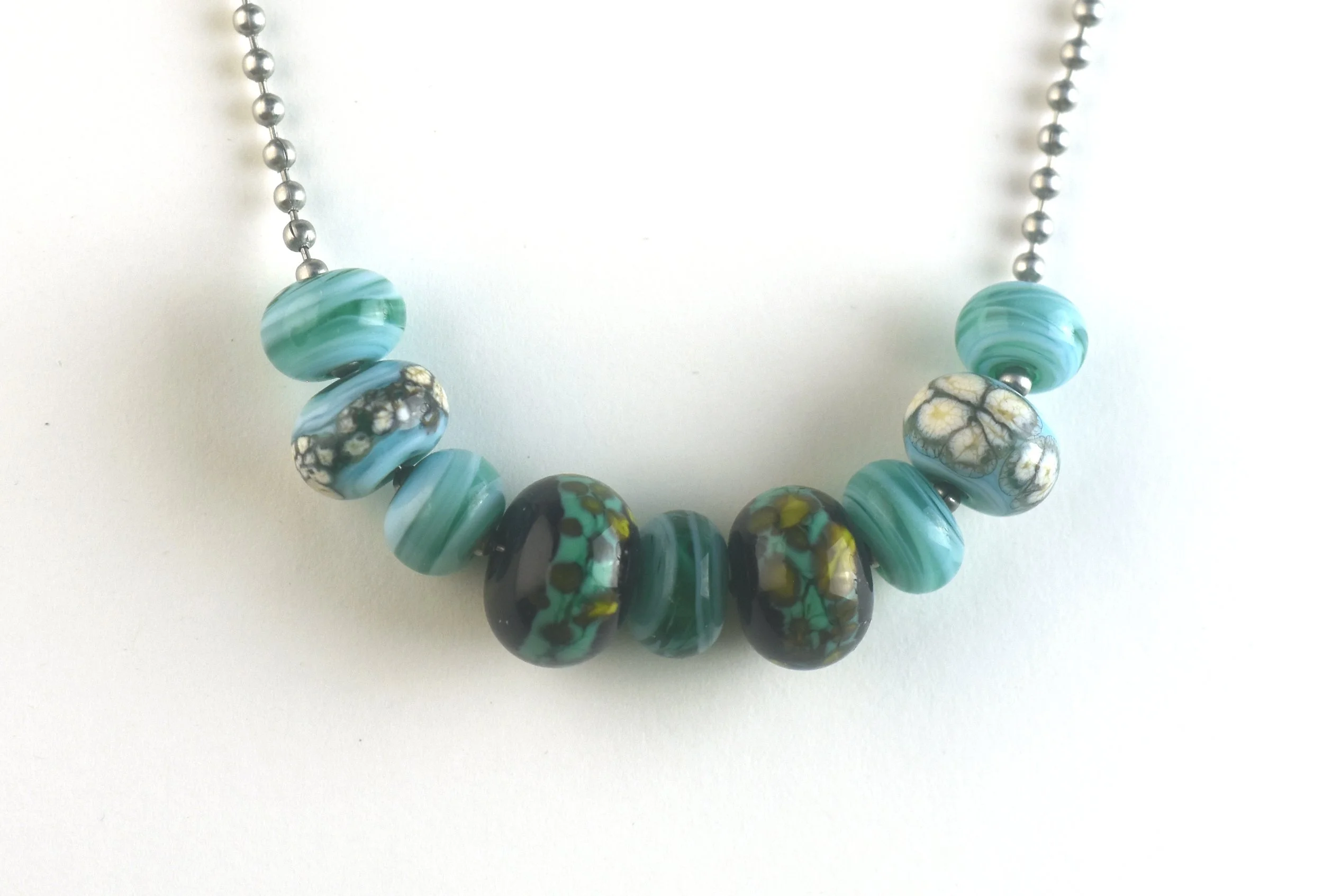 Close-up of a necklace with blue and black marbled beads and small silver spacer beads on a white background.
