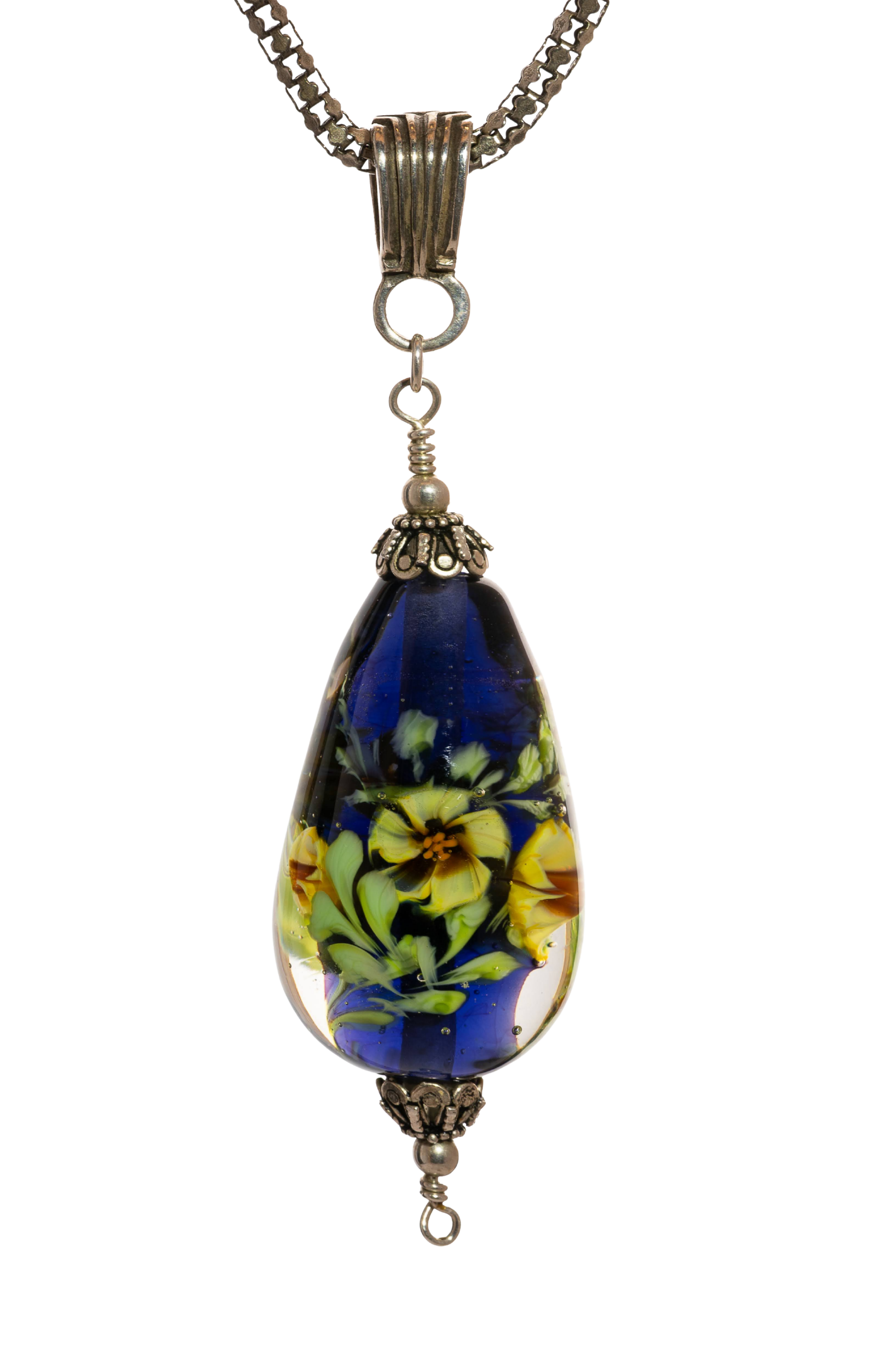 Pendant necklace with a teardrop-shaped glass bead featuring a floral internal design in yellow, white, and green hues, attached to a metal chain with decorative elements.