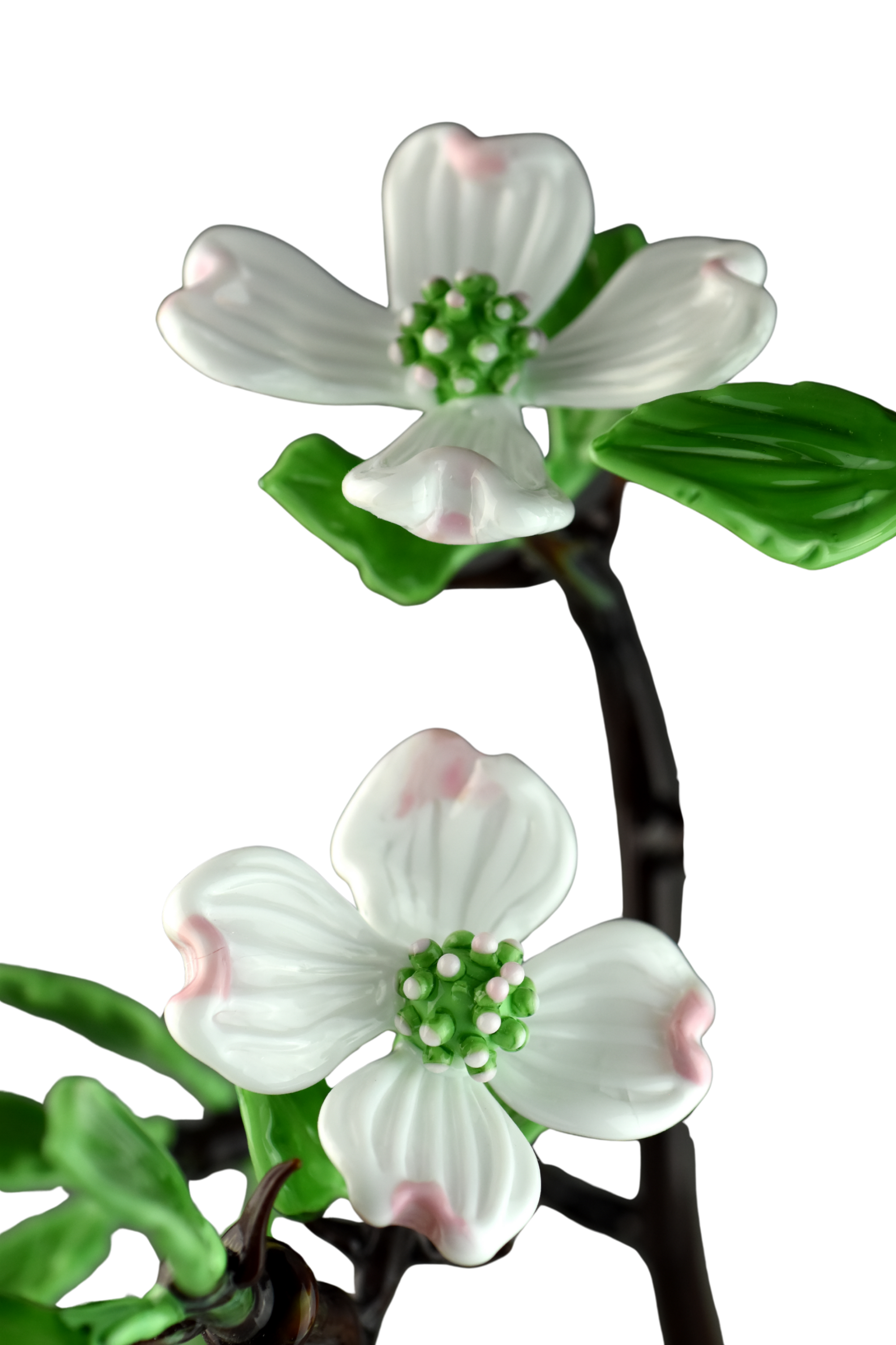 A close-up of white artificial flowers with pink accents, green leaves, and a black stem, on a black background.