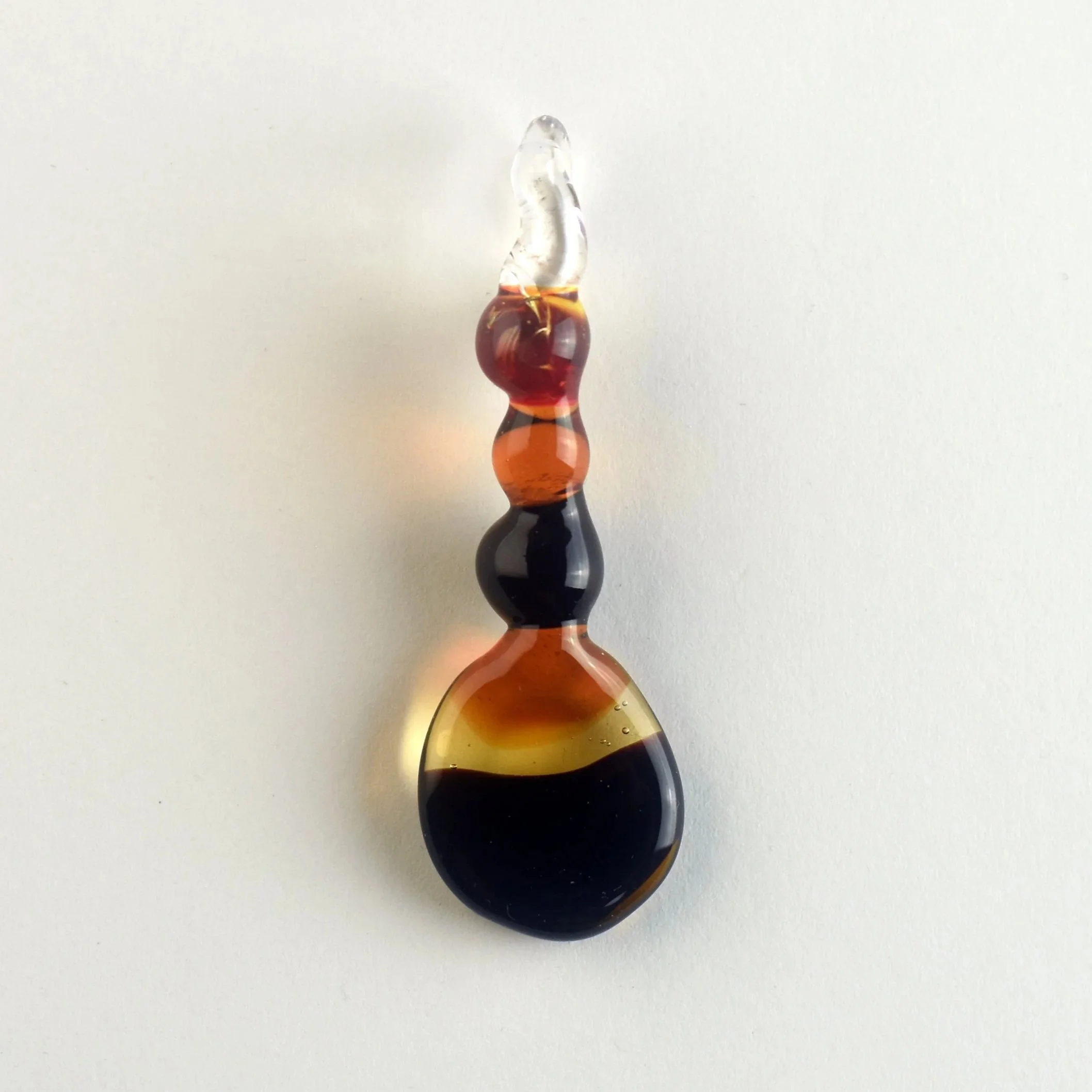A multicolored glass sculpture with a curved shape, featuring amber, black, and clear glass sections, positioned against a plain white background.