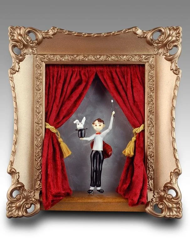 A quirky puppet show scene with a puppet dressed as a magician, holding a magic wand and a small white dove, framed by ornate gold and beige decorations with red velvet curtains.