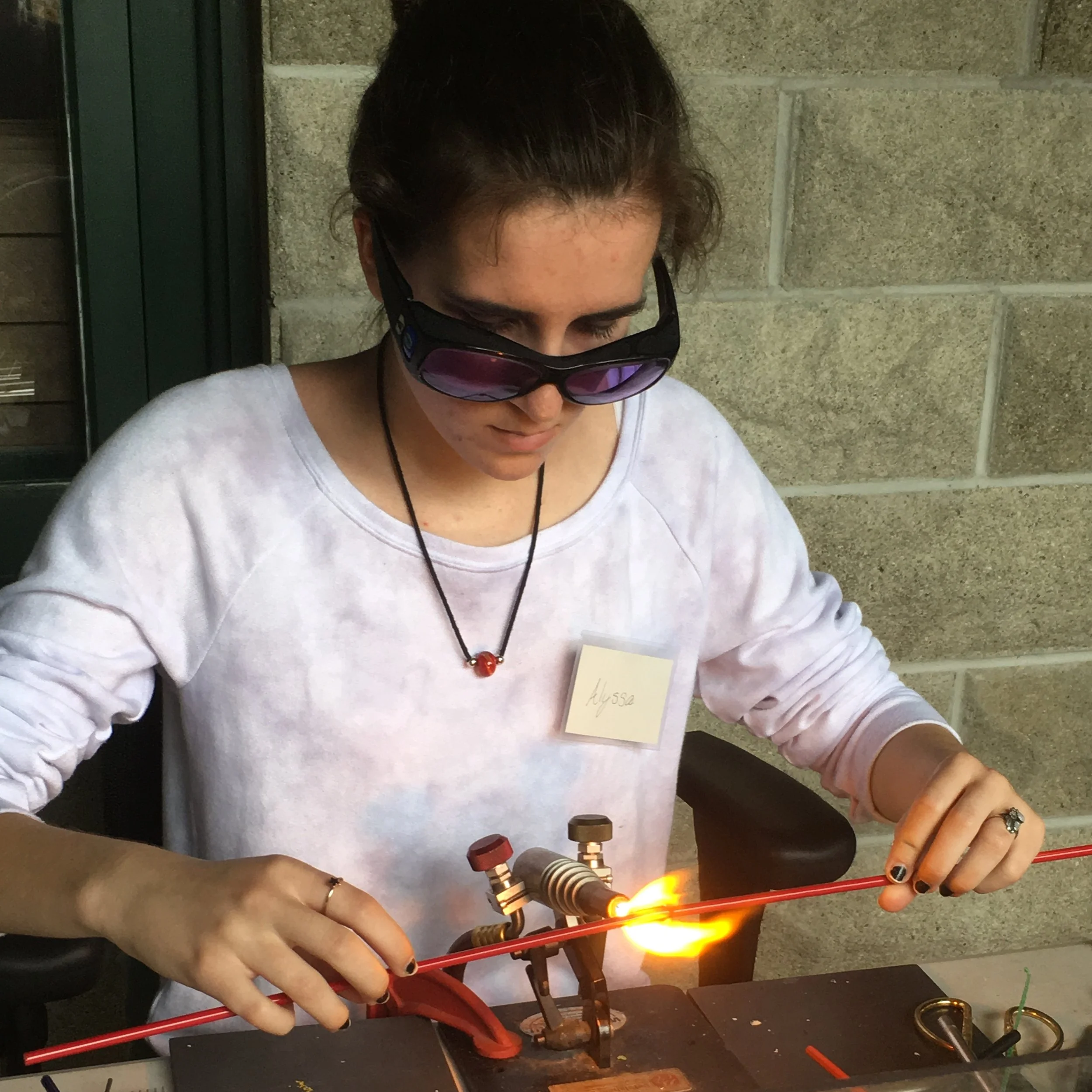 Person wearing sunglasses working with a torch and metal pipes on a workbench.
