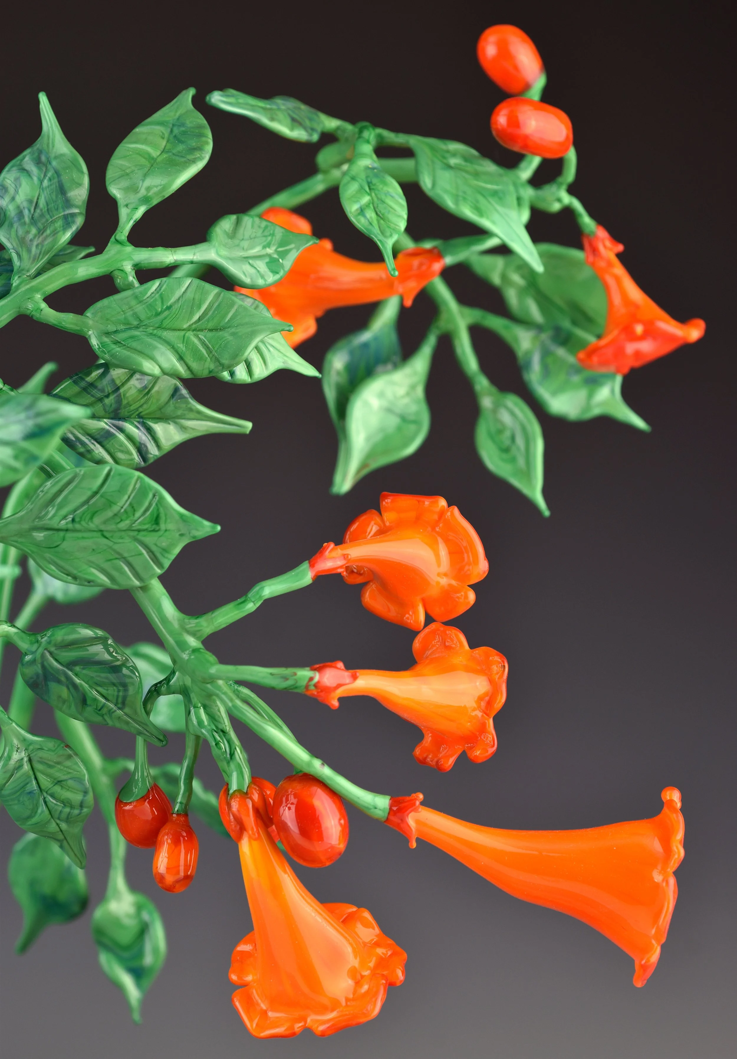 Colorful glass sculpture of a flowering plant with orange flowers, green leaves, and a dark background.