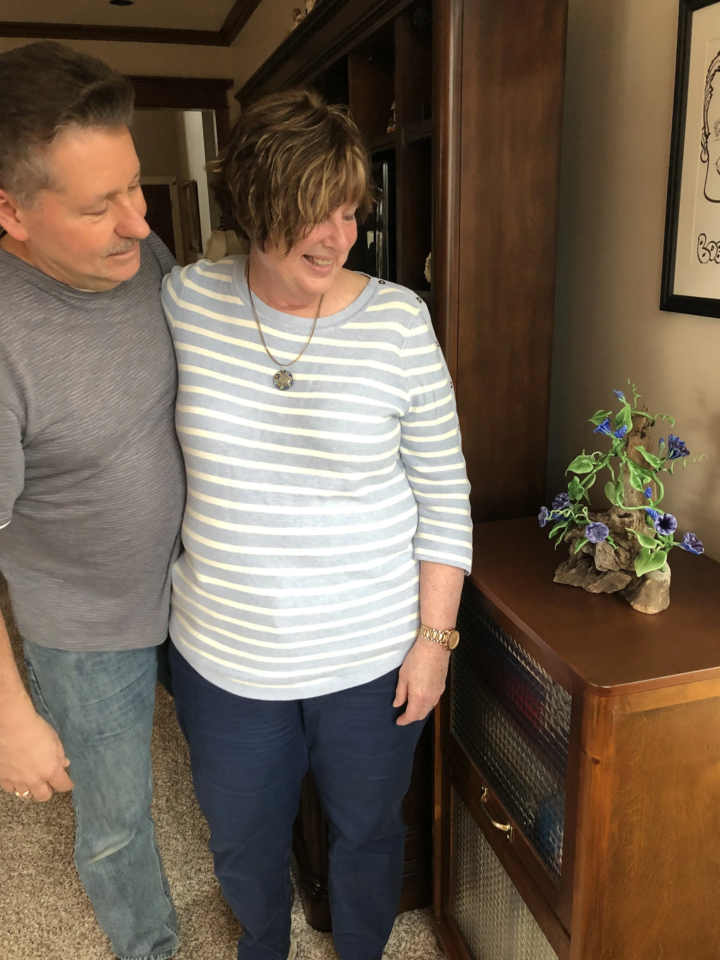 A man and a woman standing next to each other looking at a decorative plant on a wooden cabinet, in a home setting.