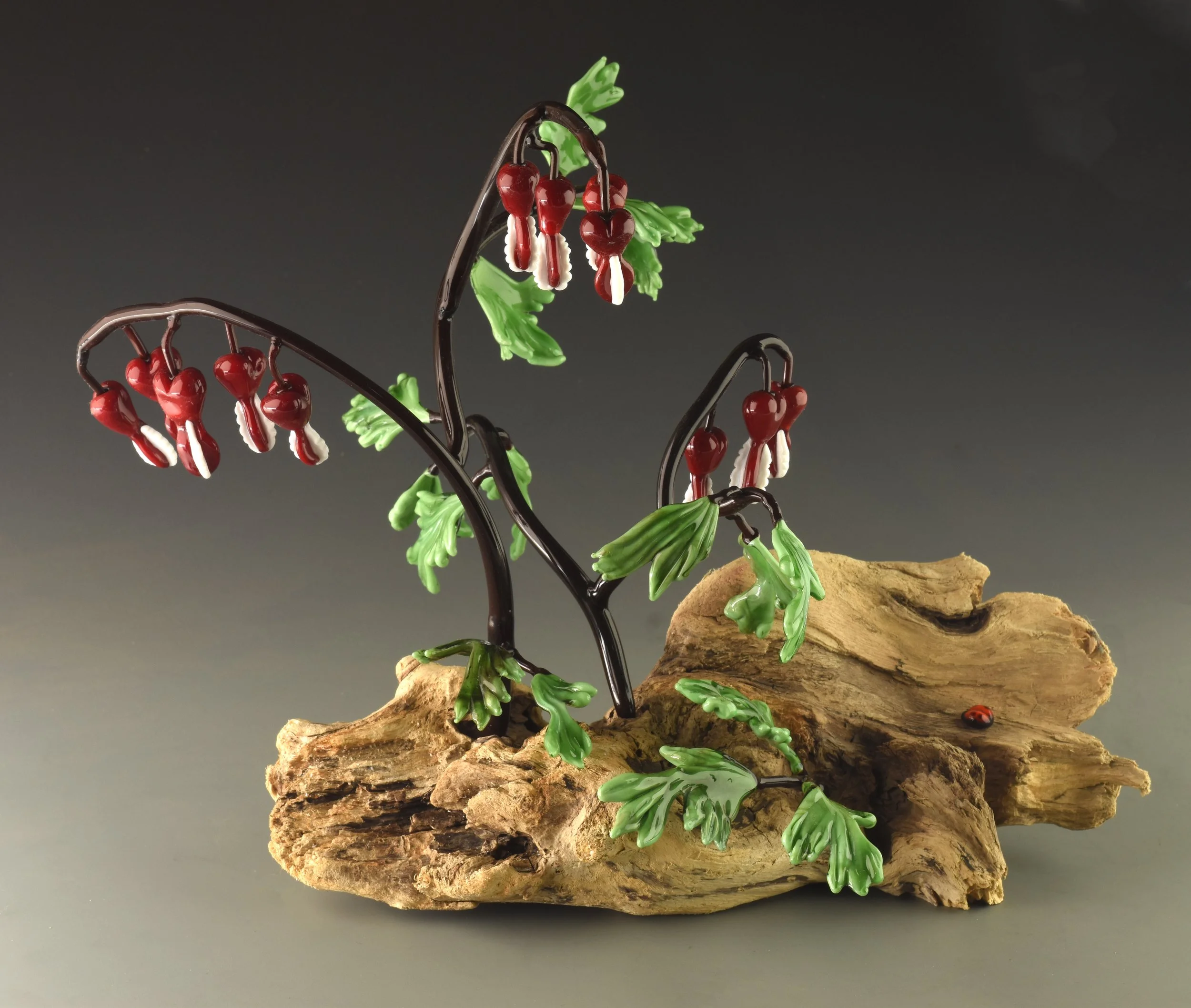 Decorative glass sculpture of red berries with white tips, green leaves, and brown branches on a piece of textured wood.