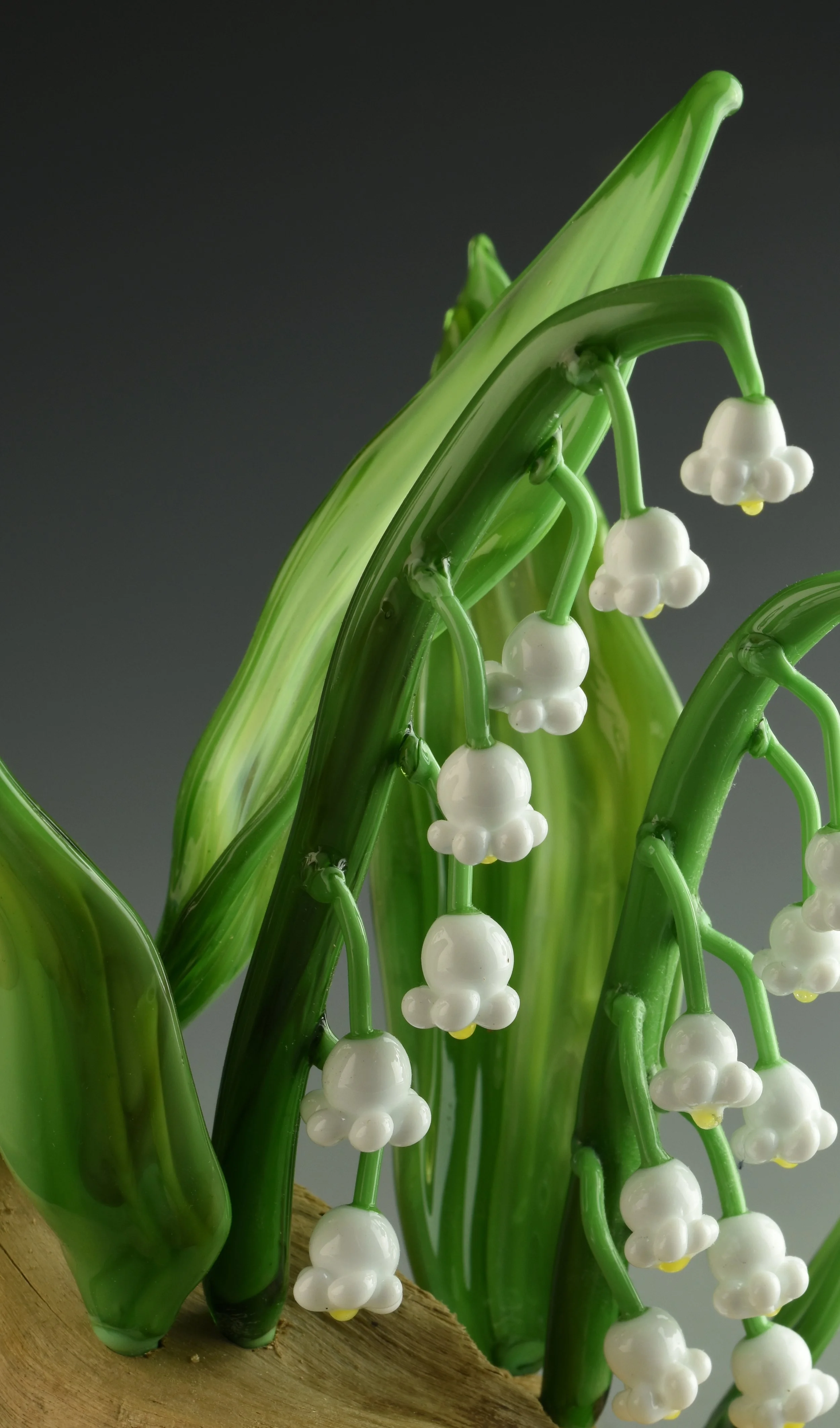 Close-up of decorative glass lily of the valley flowers with green stems and white bell-shaped blooms on wooden surface.