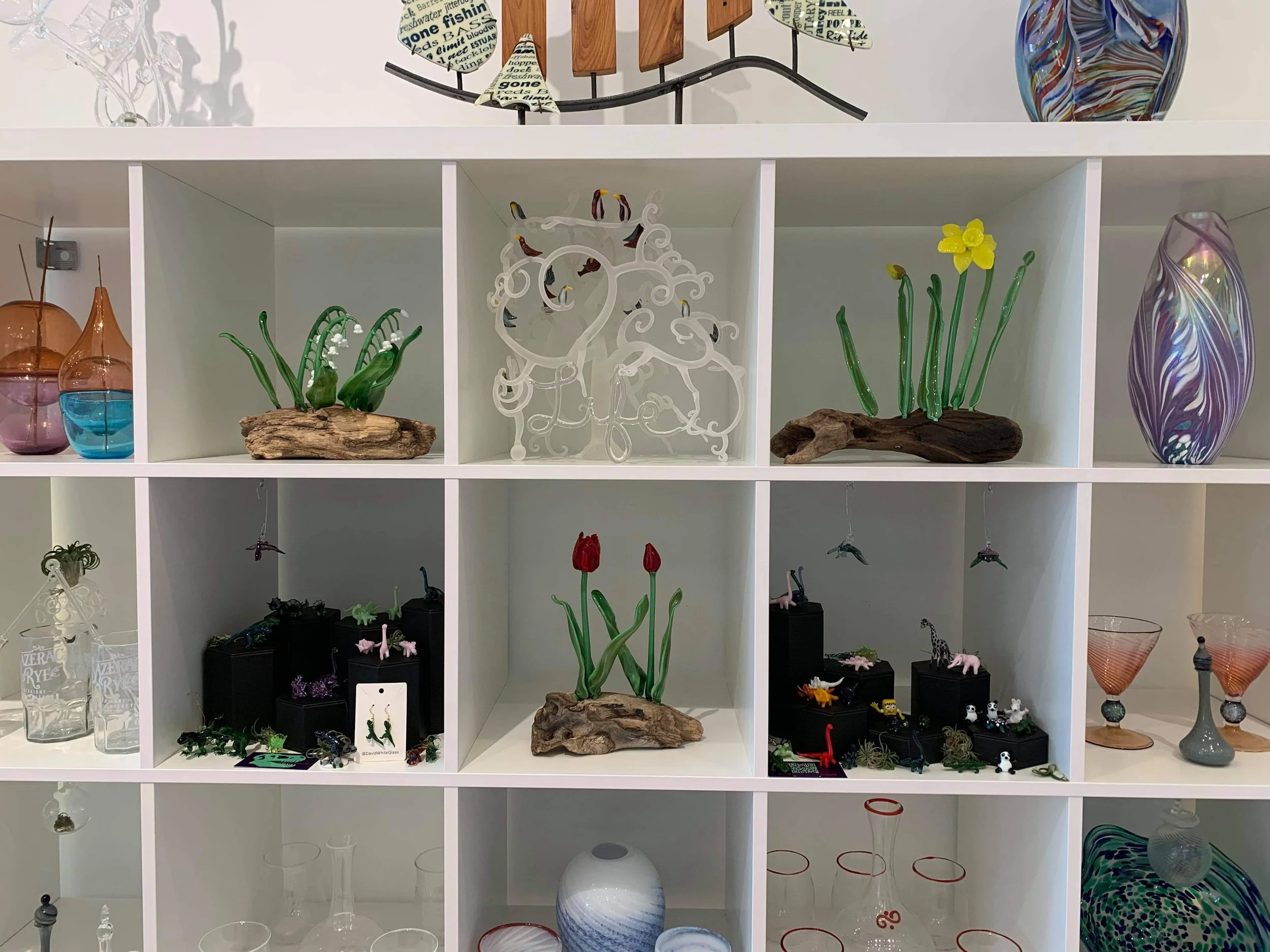 A white shelving unit with various glass and decorative items including vases, sculptures, and figurines, arranged on multiple shelves.