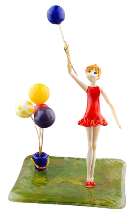 A figurine of a girl in a red dress holding a blue balloon, with a cluster of colorful balloons on sticks, standing on a green square base.