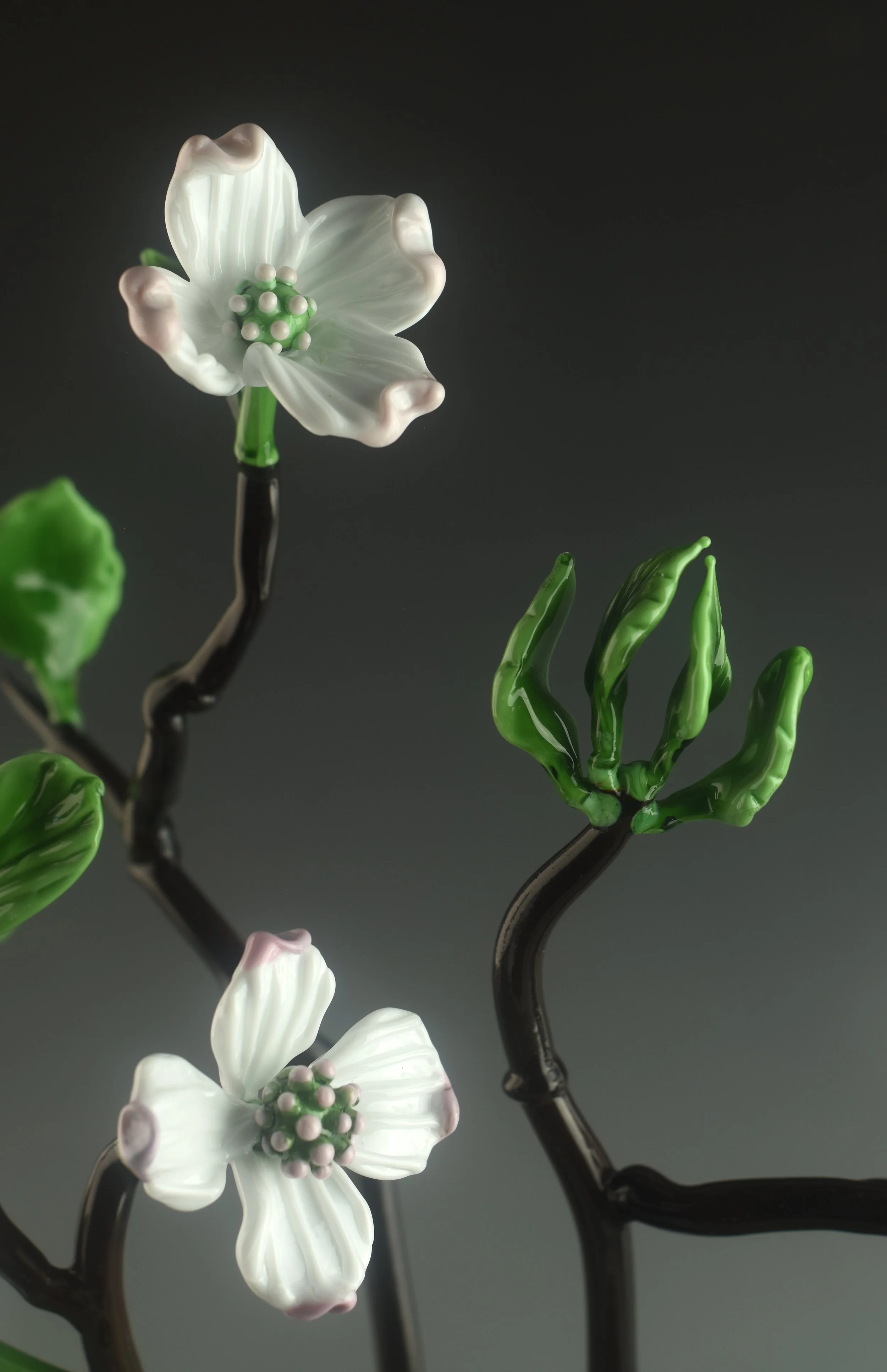 Glass sculpture of white flowers and green leaves on black stems against a dark background.