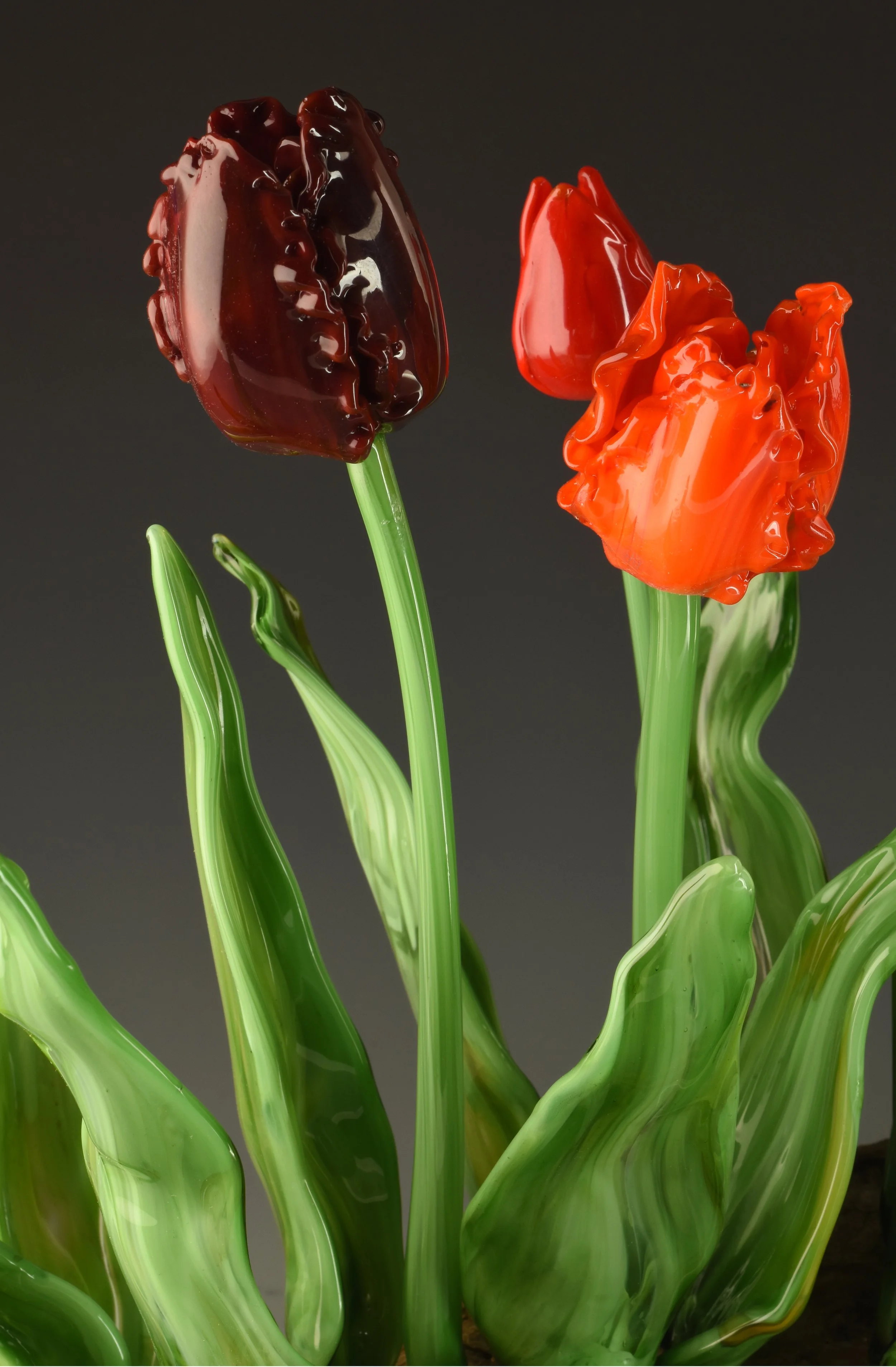 Colorful glass tulips with green stems and leaves against a dark background