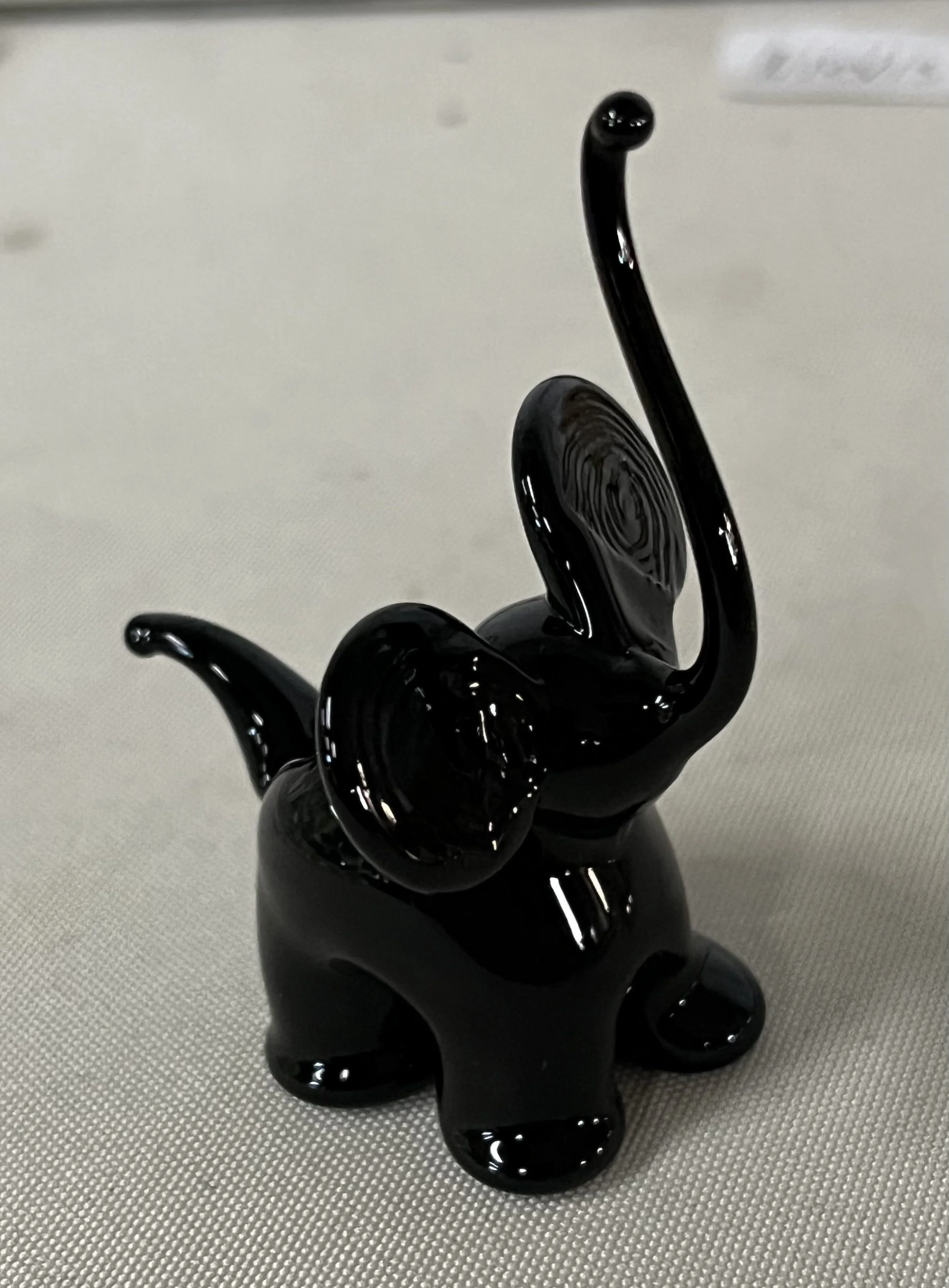A black glass sculpture resembling a snail with its shell and extended tentacles, placed on a textured gray surface.