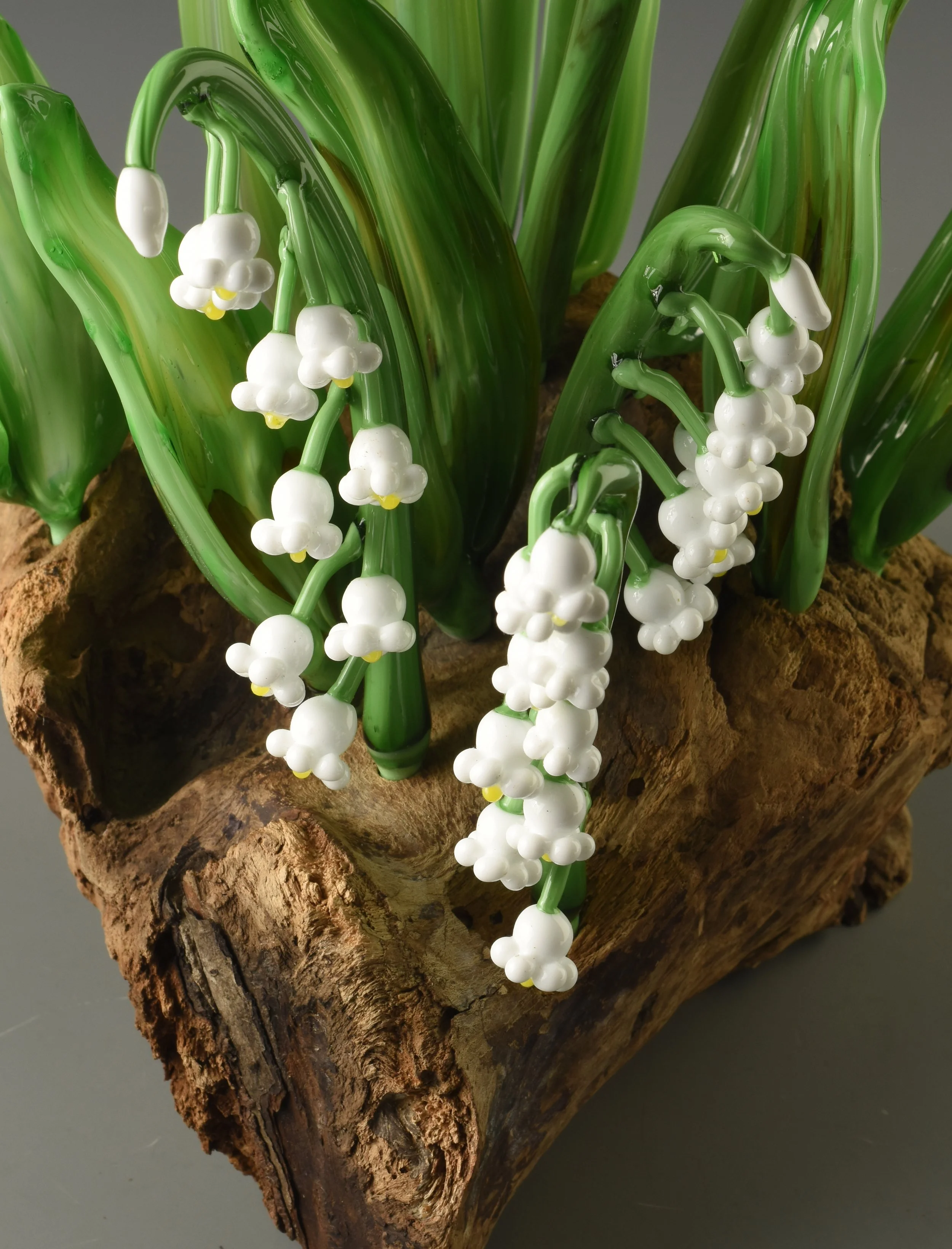 Artificial lily of the valley flowers with white bell-shaped blooms and green leaves, placed on a piece of rustic wood.