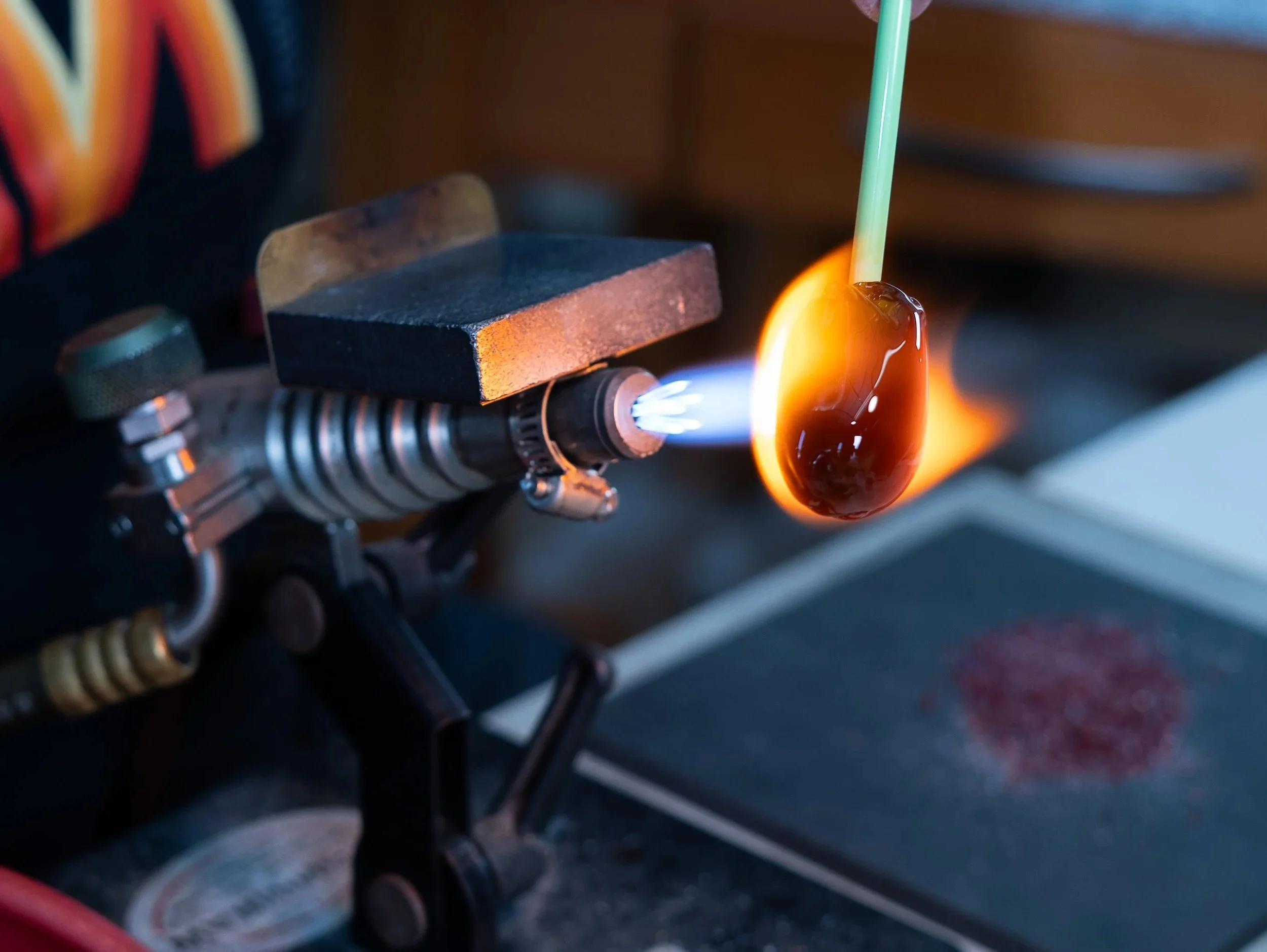 A close-up of a glassblowing process where molten glass is being shaped using a blowtorch and tools.
