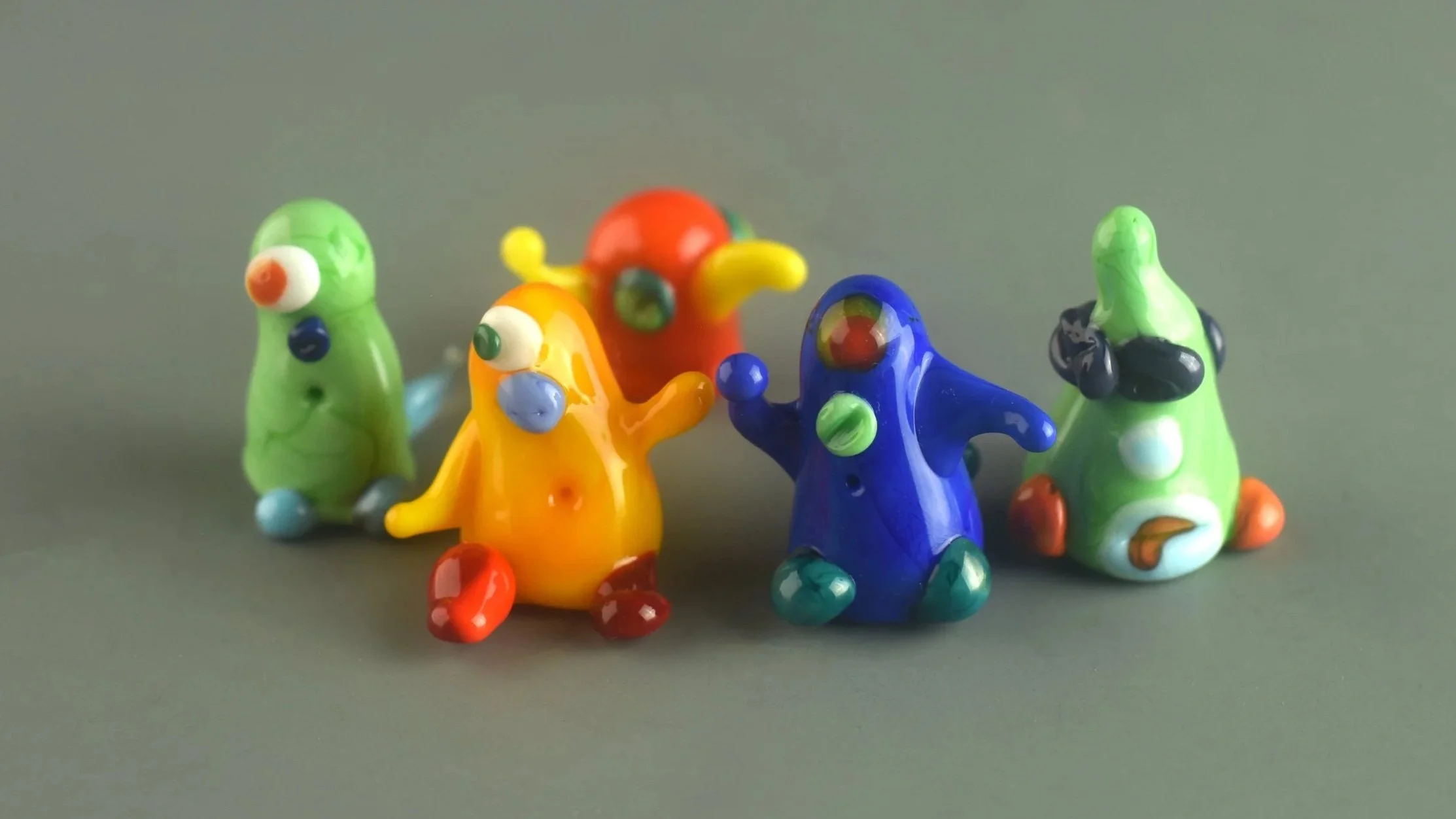 Colorful glass mouse figurines with round eyes and different patterns on a gray surface.