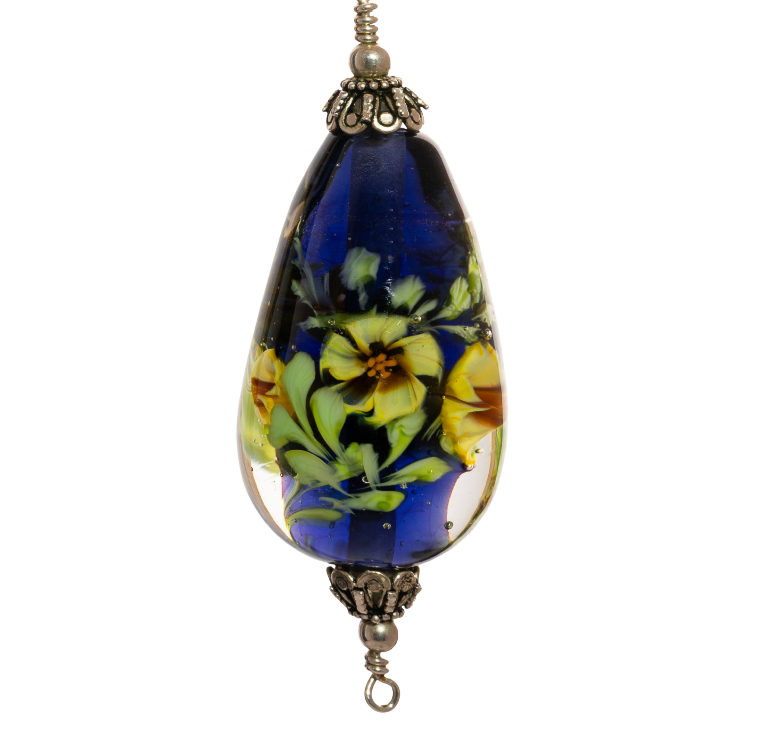 Close-up of a decorative glass murrini bead with blue, green, and yellow floral patterns, featuring a metal hook at the bottom.