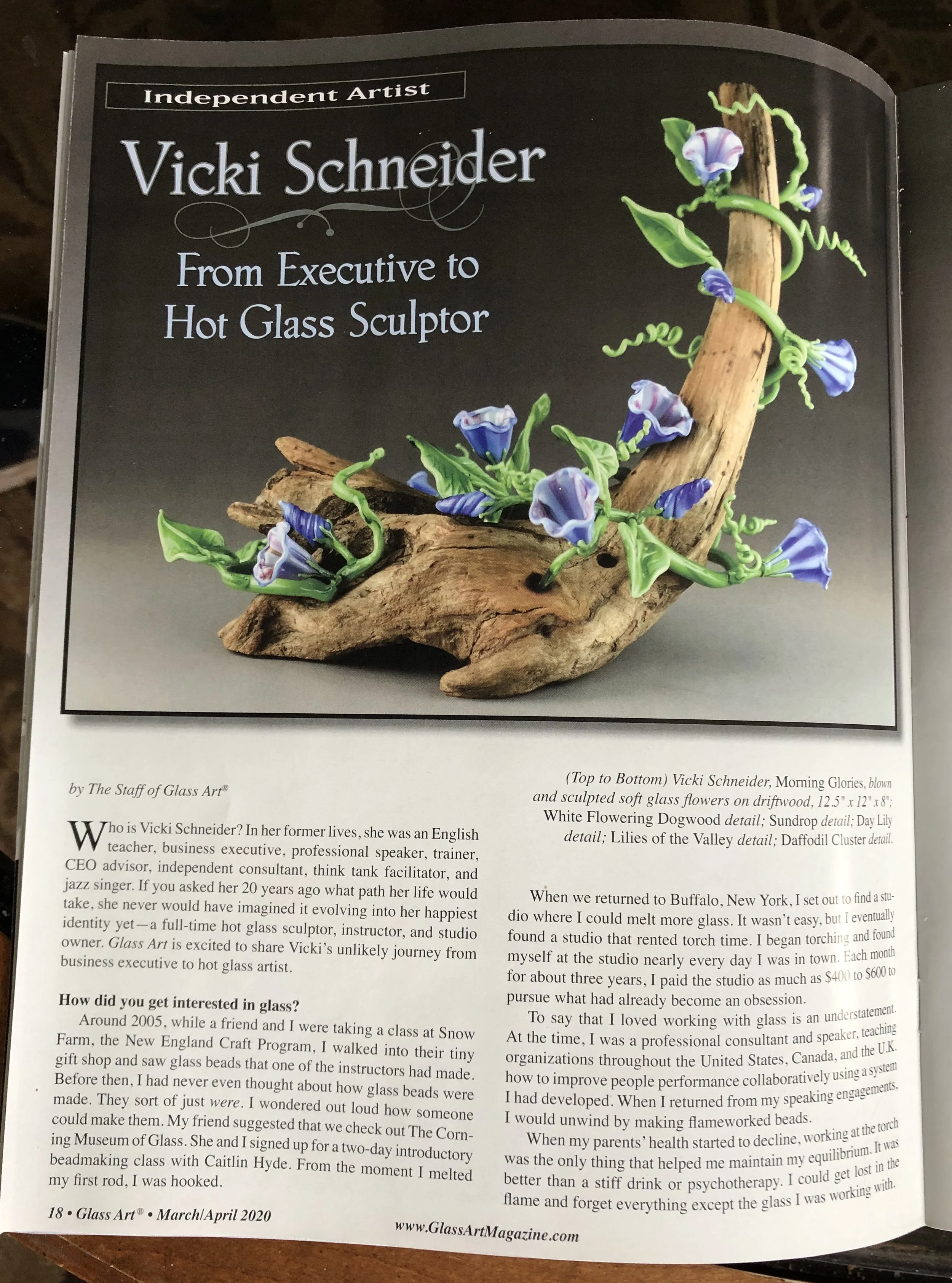 A magazine article featuring a gift piece of glass art, a sculpture of a driftwood branch with blue and purple glass flowers and green glass vines.