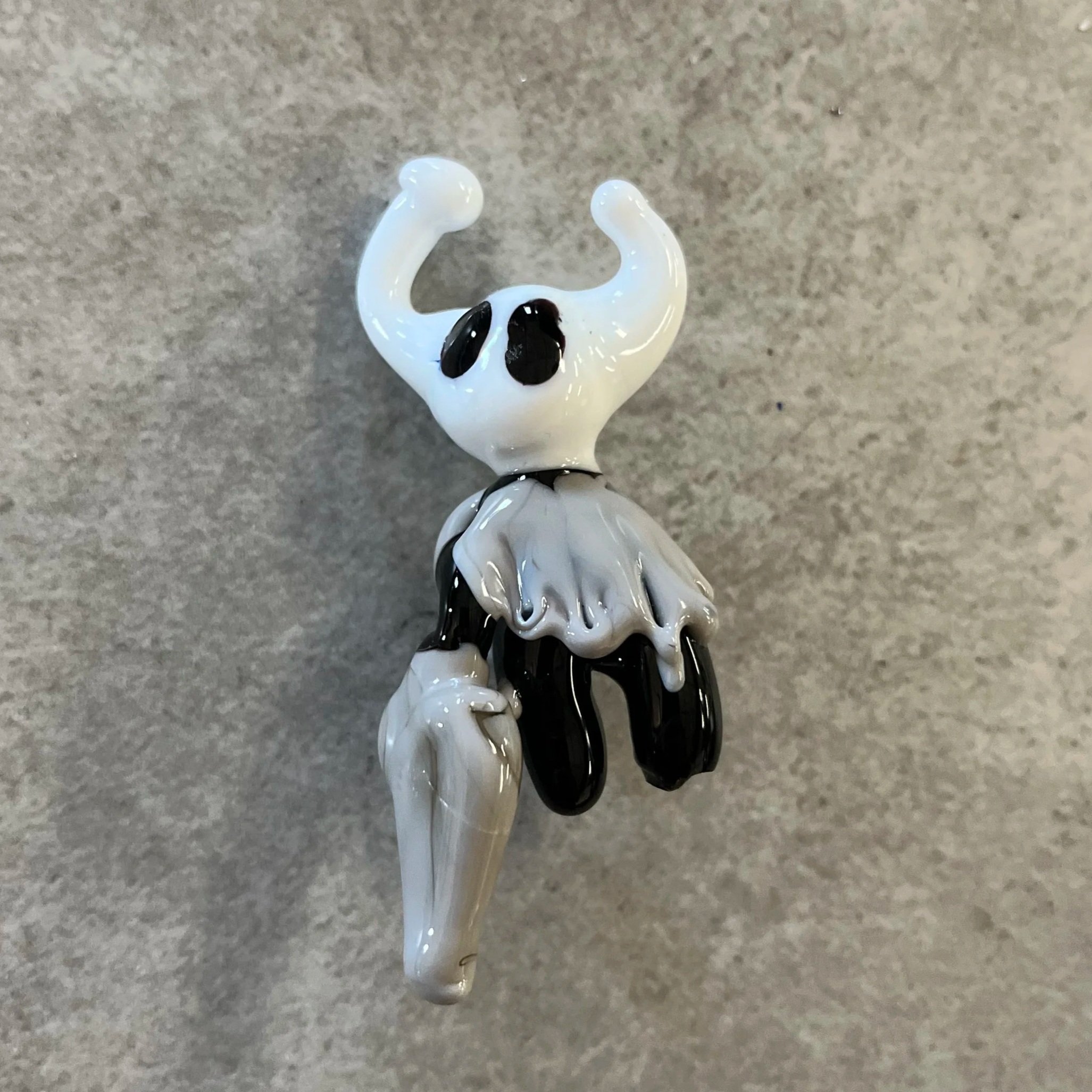 A glass figurine of a cat with black eyes and a tail, positioned on a gray surface.