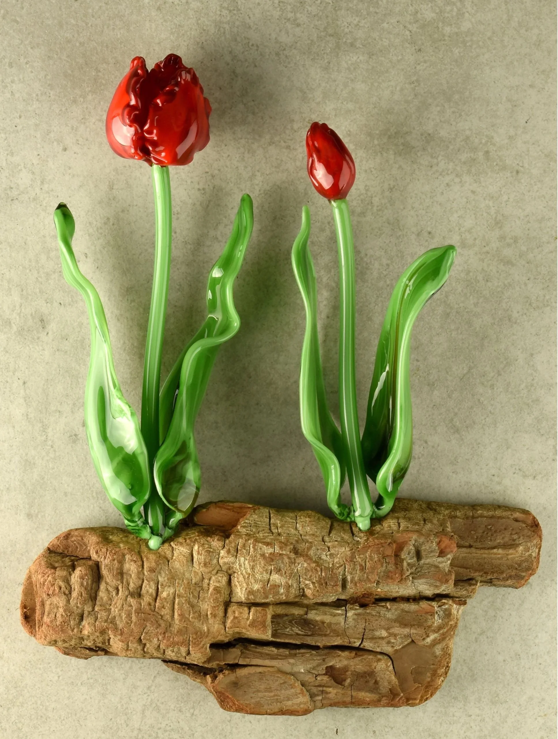 Glass sculpture of red tulip flowers with green stems, mounted on a piece of bark.