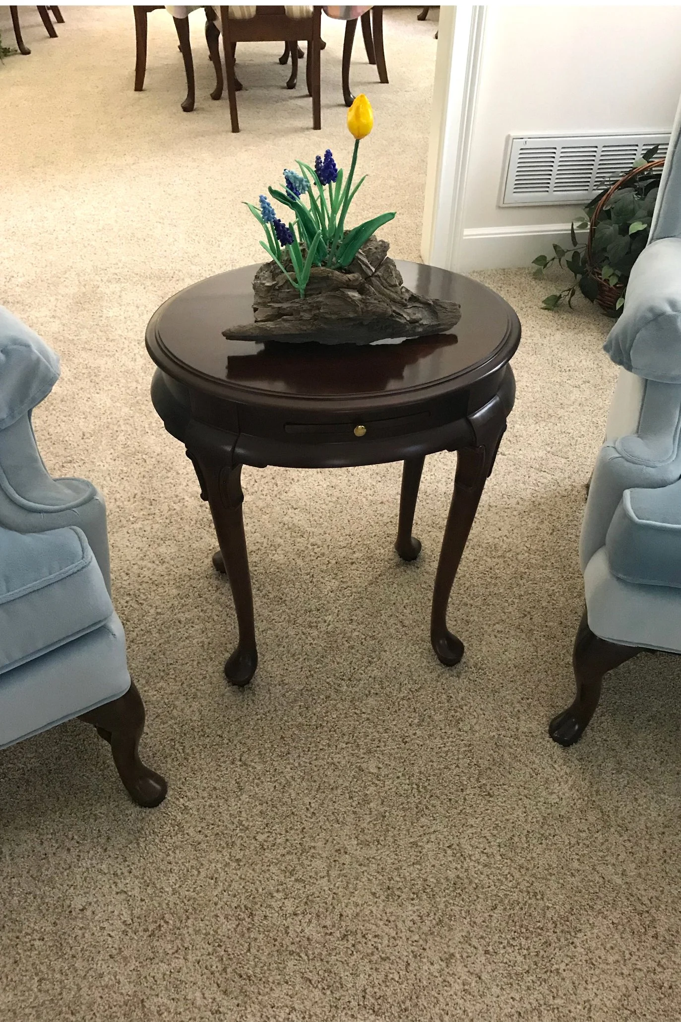 A wooden side table with a flower arrangement of purple hyacinths and a yellow tulip on top.