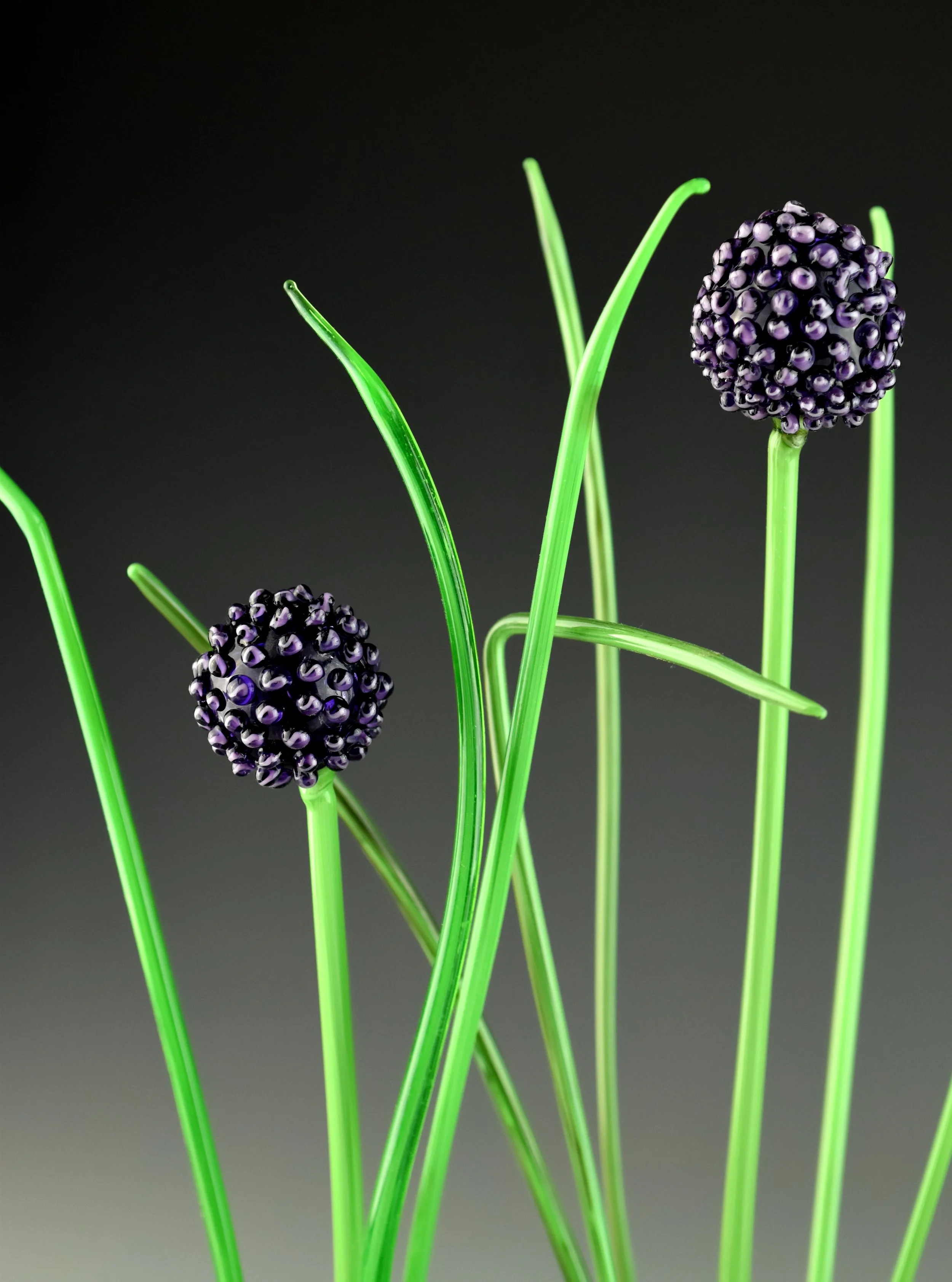 Close-up of green plastic stems with purple and black decorative flower heads against a dark background.