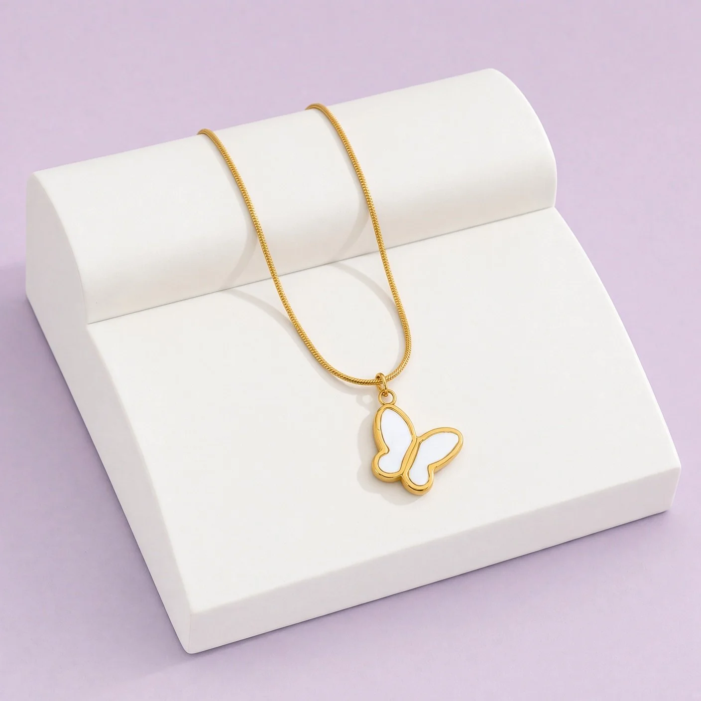 Gold snake chain necklace with white enamel butterfly pendant on white display stand