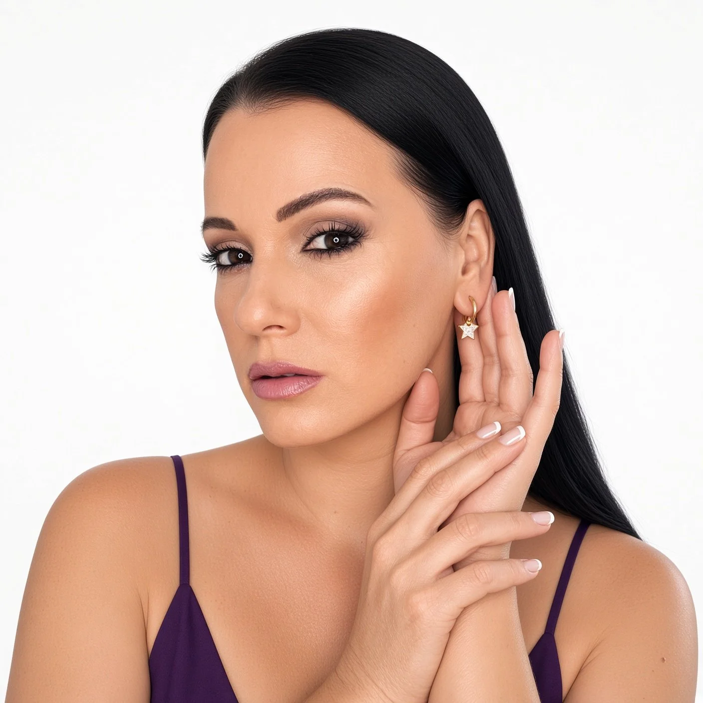 Model in purple dress wears gold star charm hoop earring, hand gently touching her face