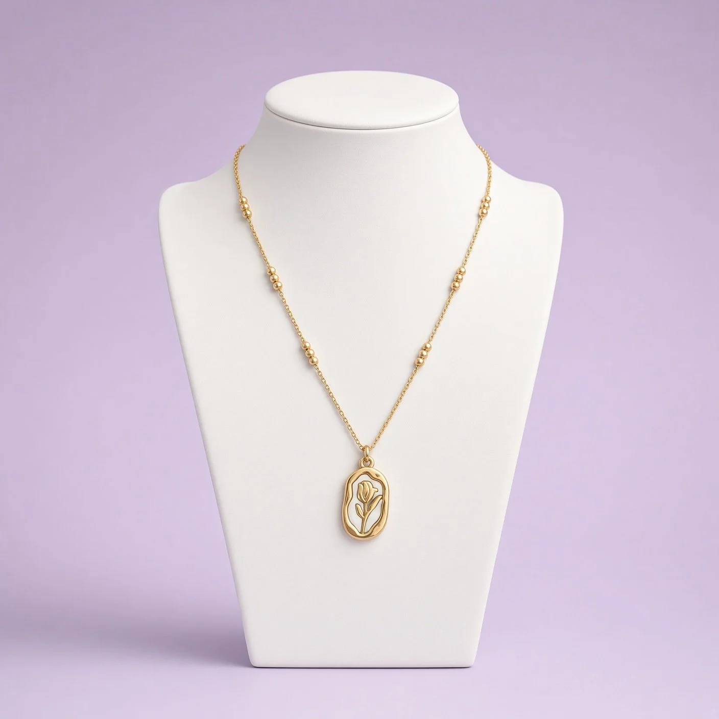 Gold-tone tulip pendant necklace with bead accents on white bust stand, lilac backdrop
