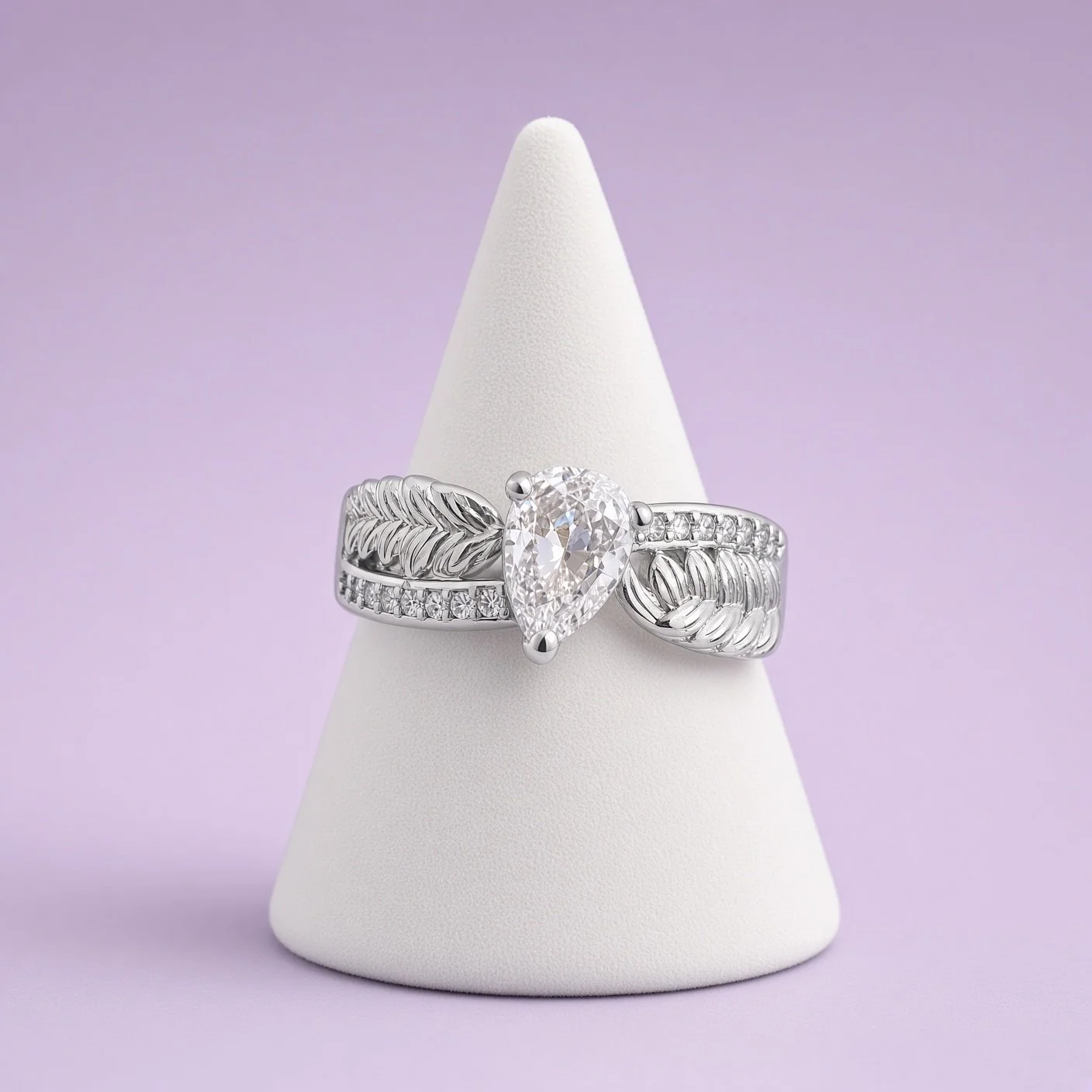 Silver-tone leaf-detail ring with large pear clear stone on white cone stand against lilac