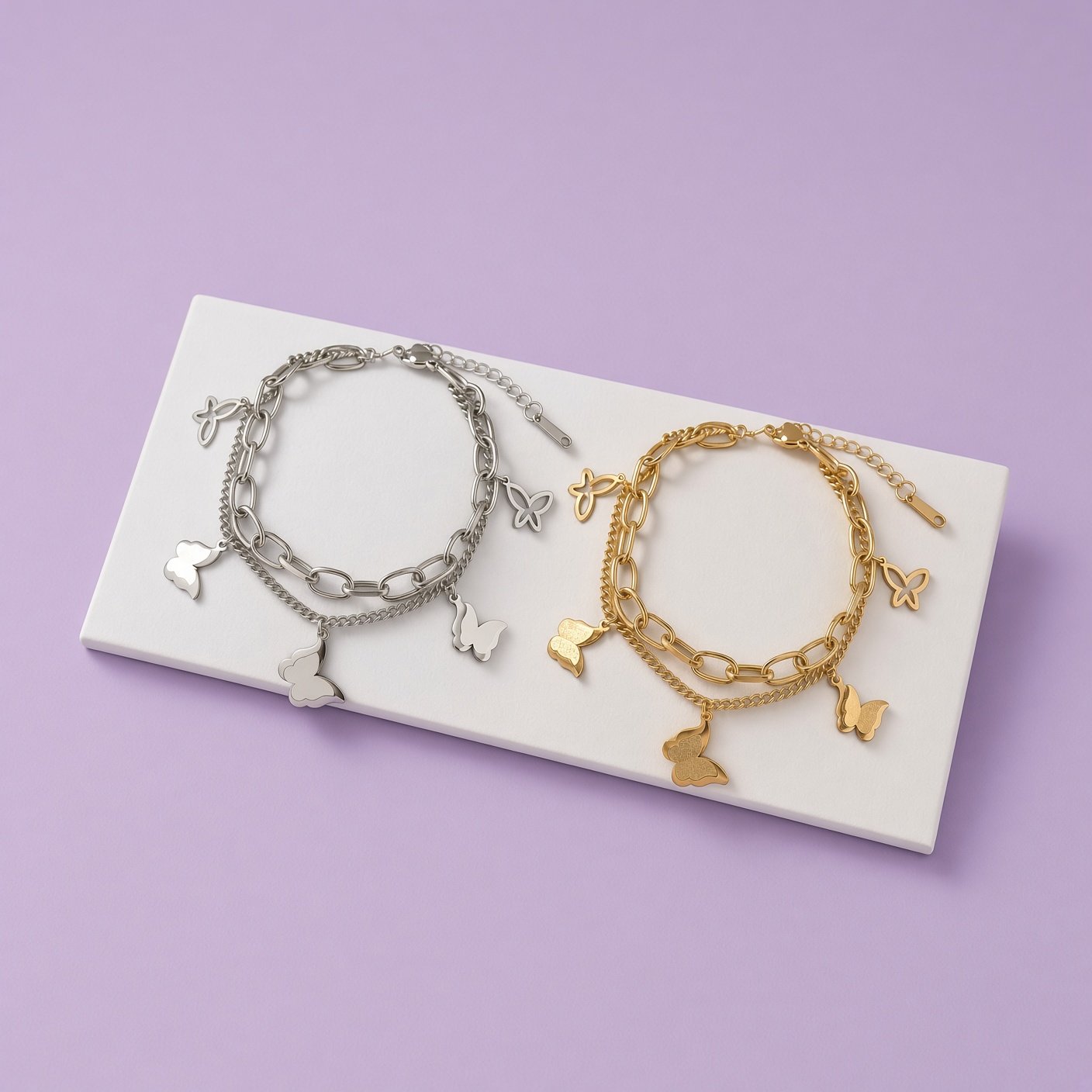 Silver-tone and gold butterfly charm bracelets side by side on white tray against lilac background