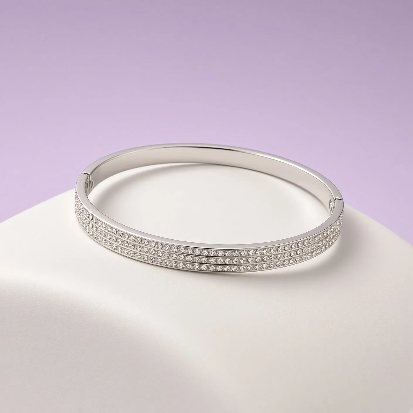 Close-up of silver-tone bangle with three rows of clear stones on white stand, lilac backdrop