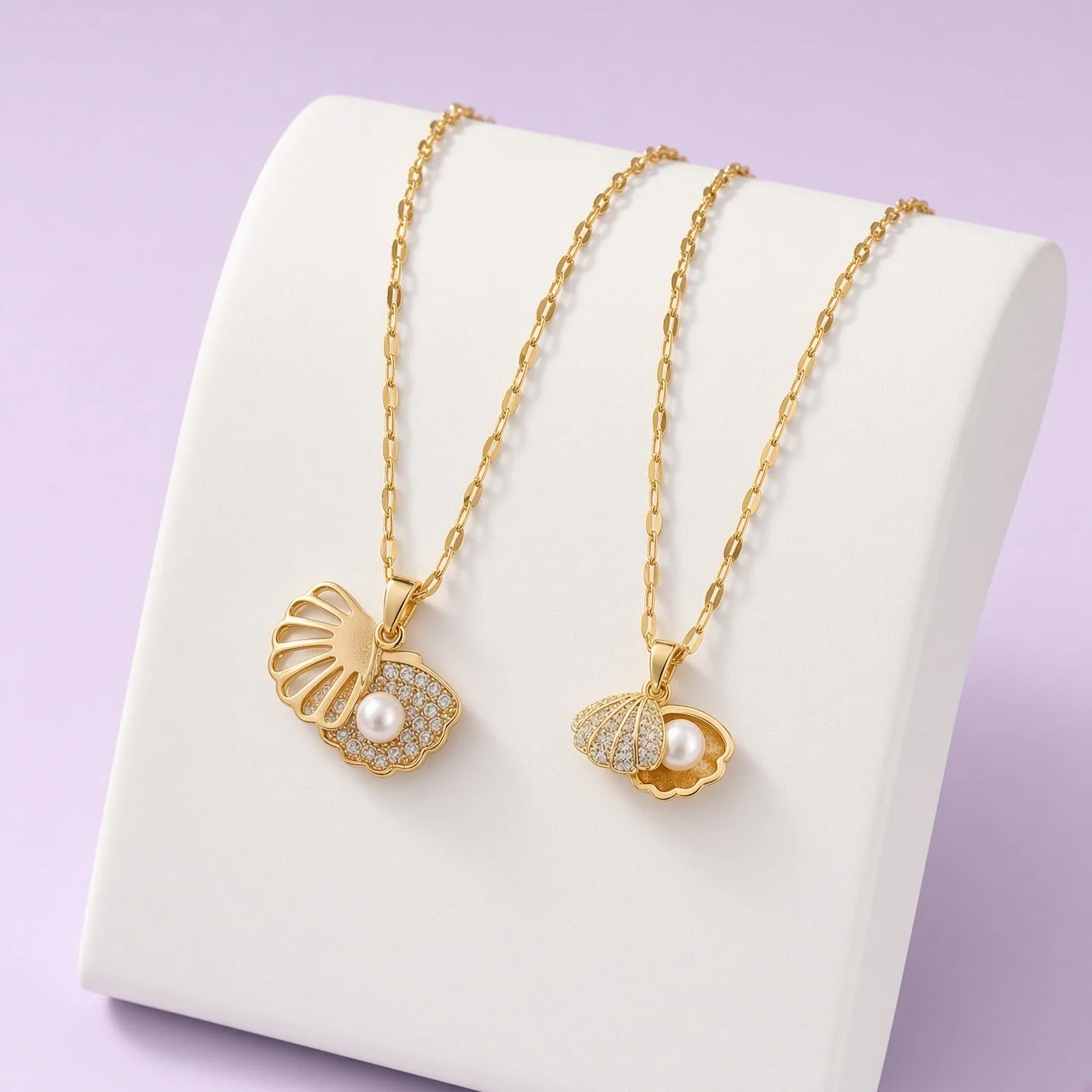 Two gold shell pendants with pearl centers on white stand against lilac background