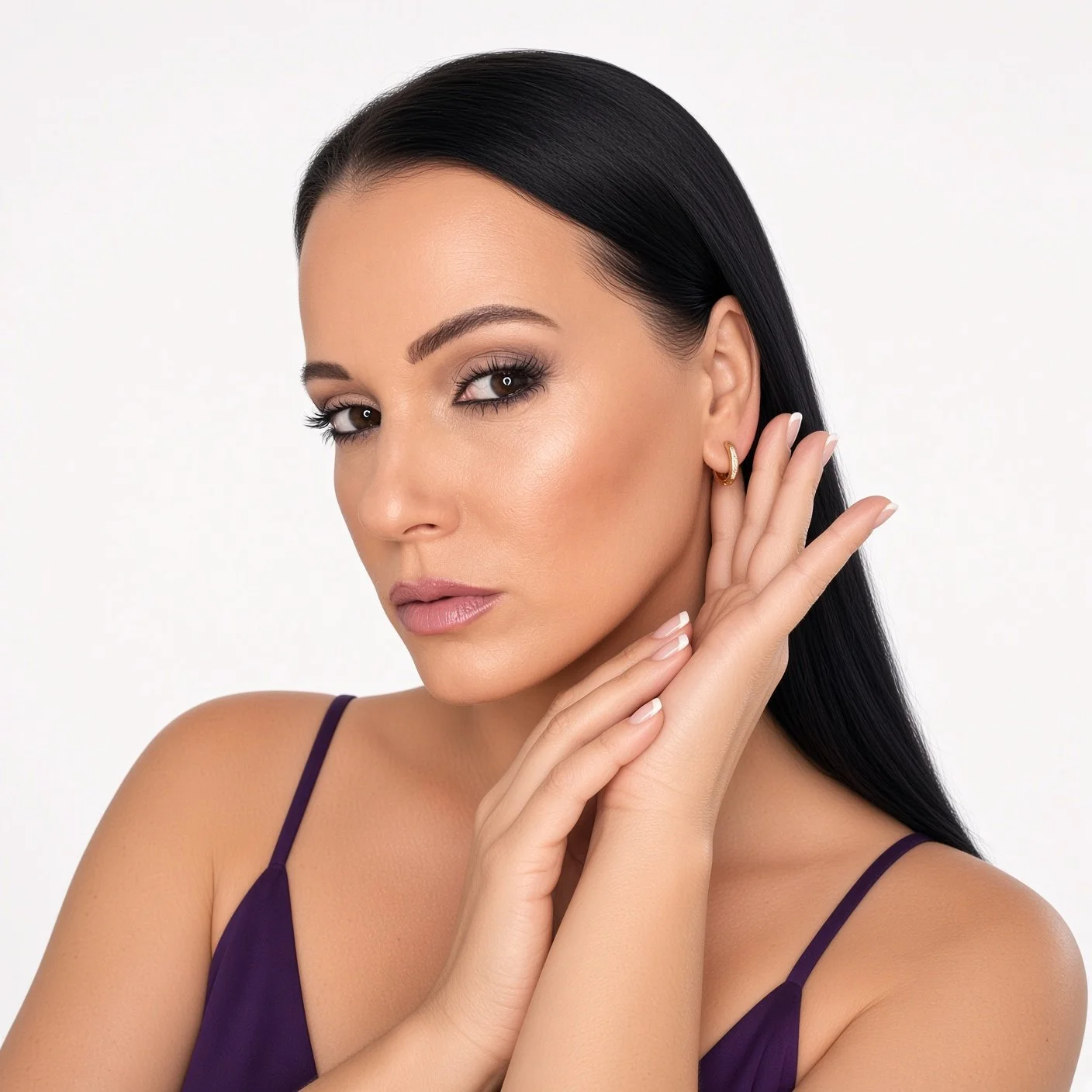 Dark-haired model models simple gold hoop earring, fingers lightly touching her neck