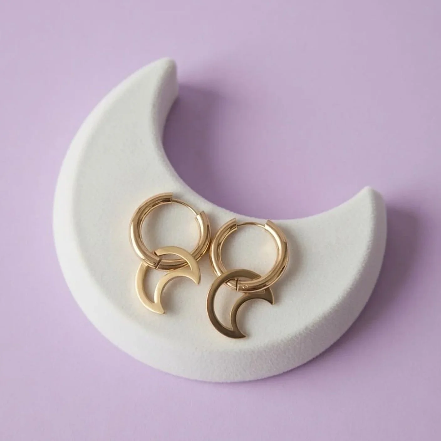 Gold-plated hoop earrings with crescent-moon charms on a white moon-shaped display