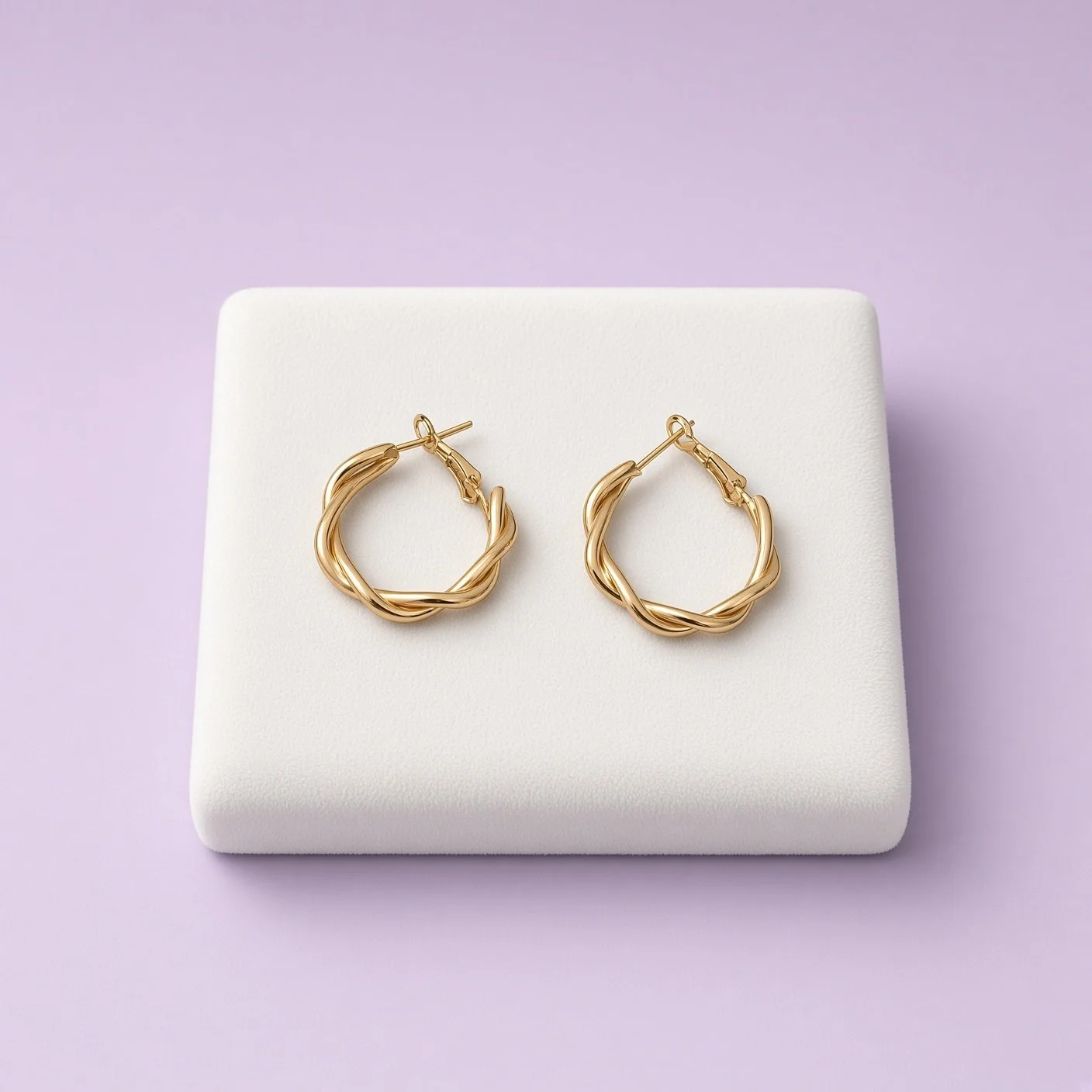 Gold-plated twisted hoop earrings on a white display pad