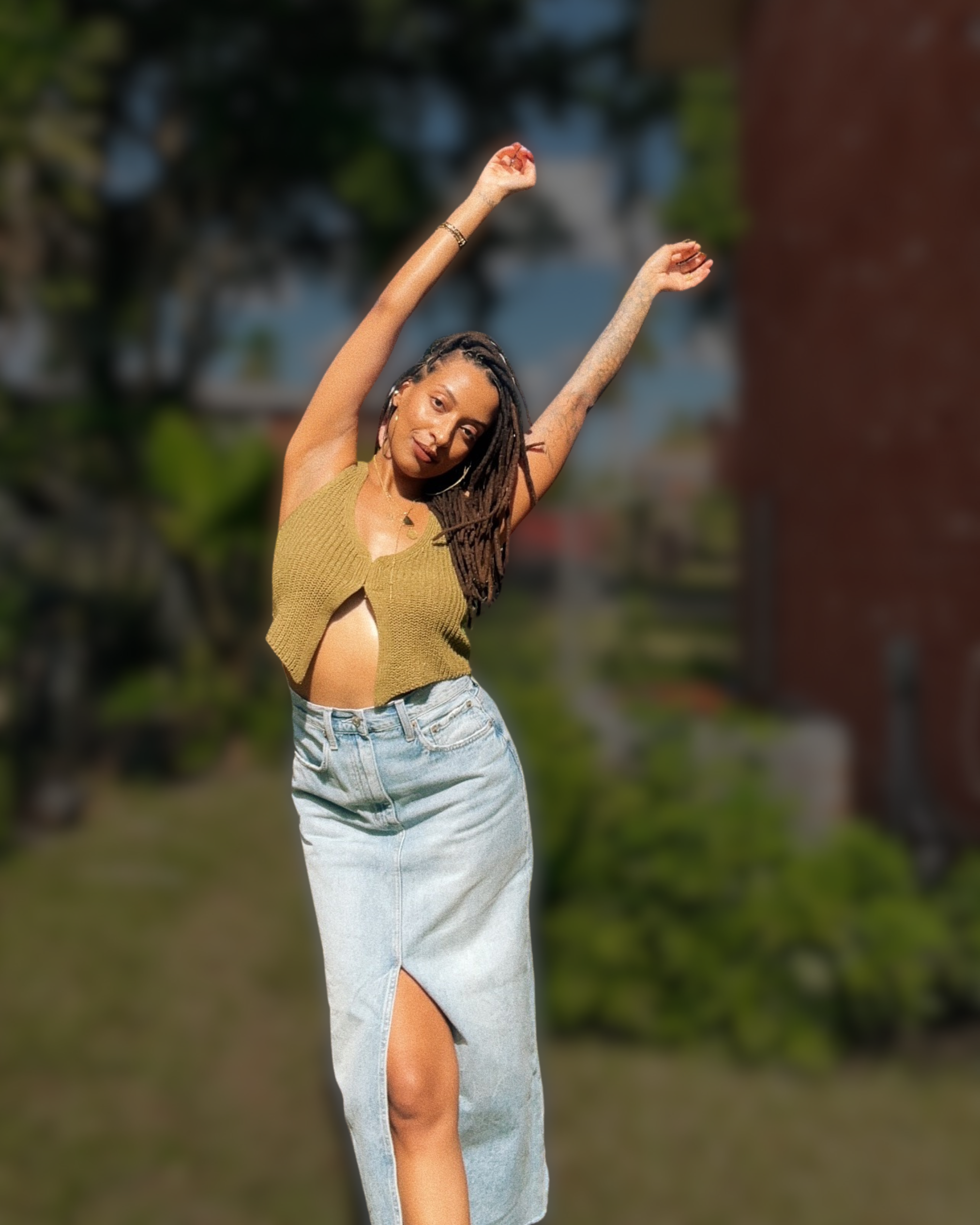 Stevie Reneé, embodiment and well-being coach, standing outdoors with arms raised in sunlight.”