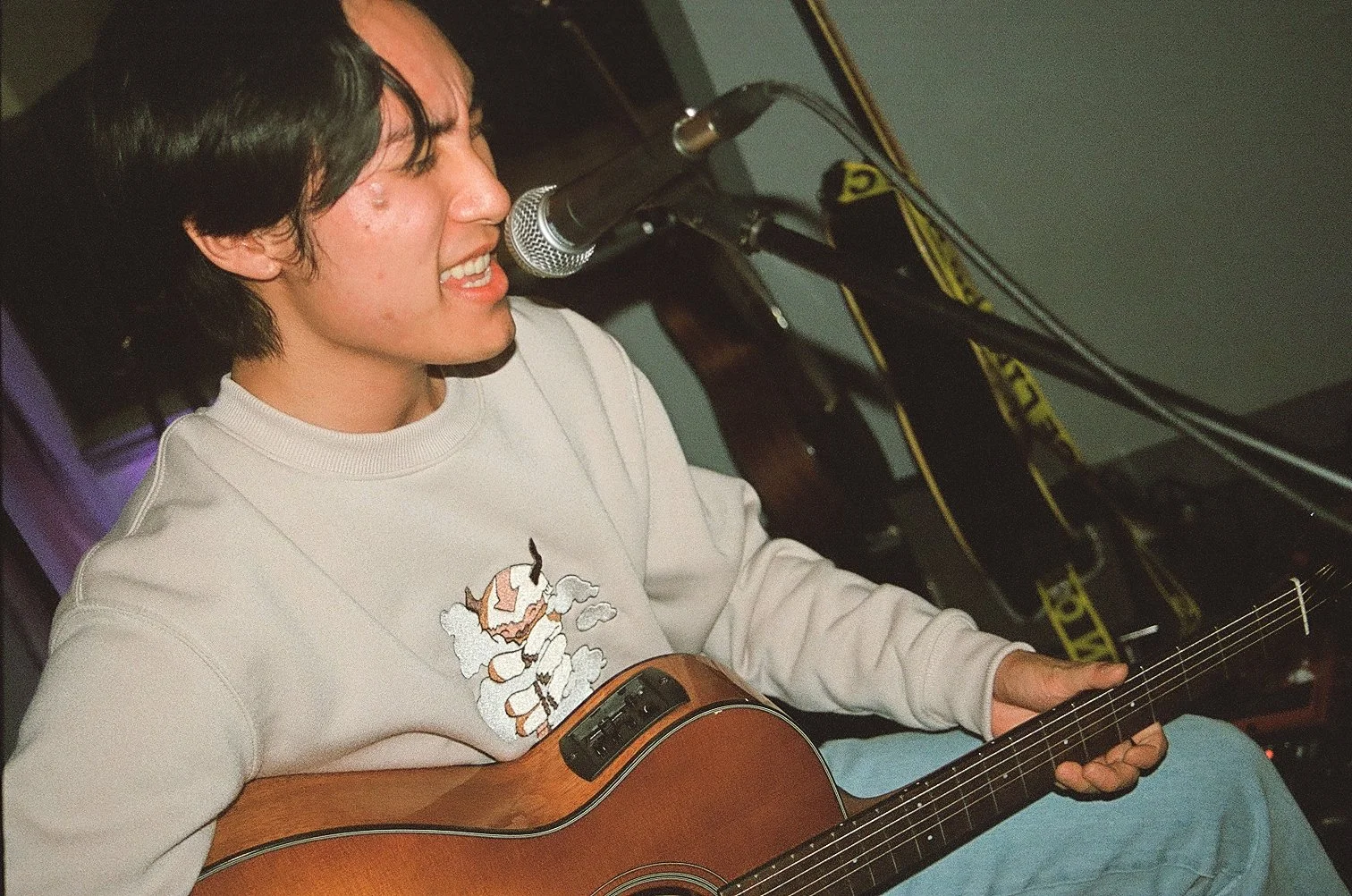 Young man singing into a microphone while playing an acoustic guitar.