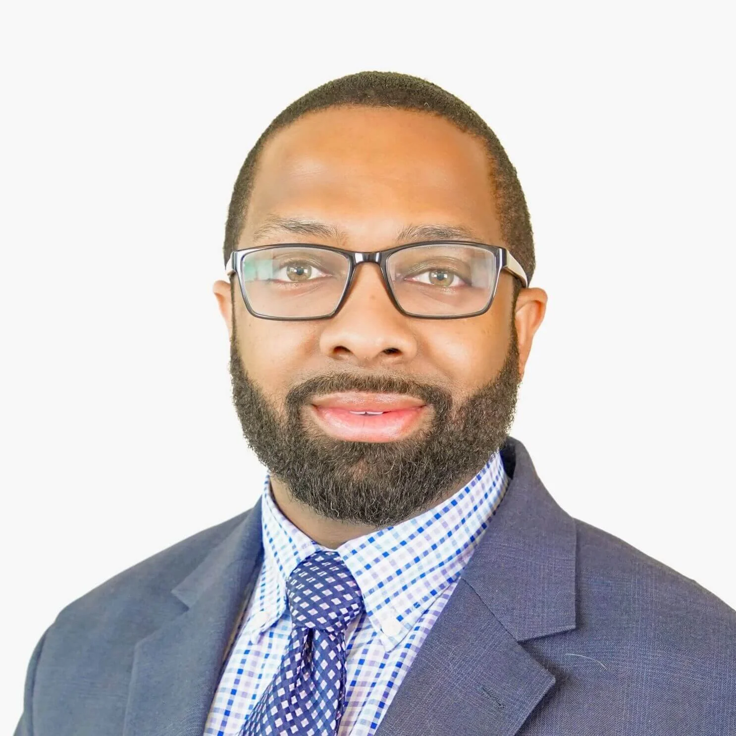 Portrait of an African American man wearing glasses, a blue suit, a checkered shirt, and a patterned tie, with a slight smile and a white background.