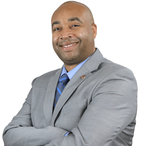 A smiling African American man wearing a light gray suit, blue dress shirt, and striped blue tie, with arms crossed against a white background.